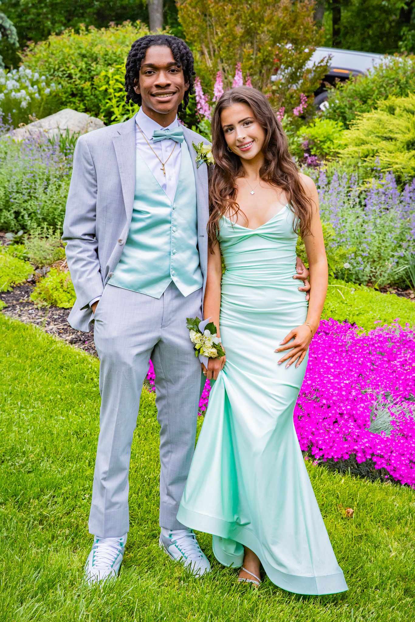 Prom couple in matching mint green outfits posing in a colorful garden setting.