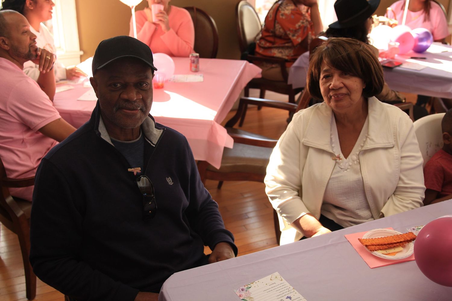 Elderly man and woman smile together at a table during a baby shower celebration.