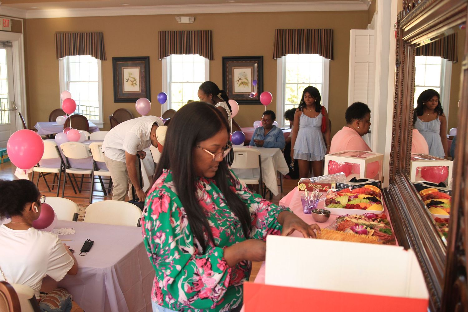 Guests browse a gift and activity table at a colorful pink balloon-decorated birthday party celebration.