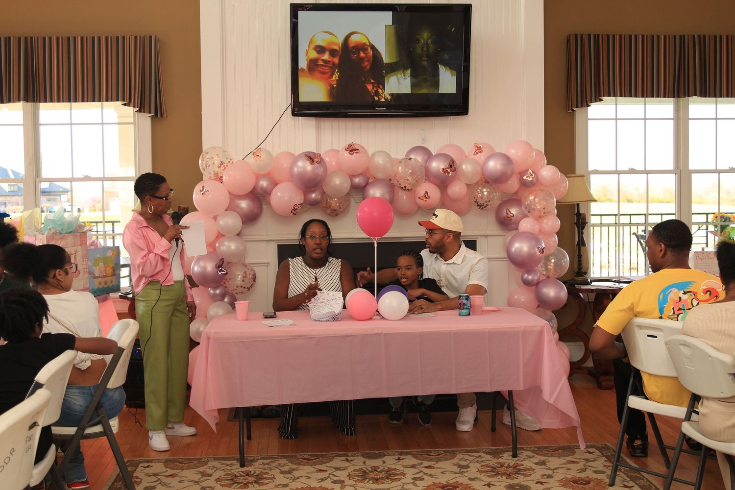 Guests gather at a baby shower with pink and purple balloon arch backdrop.