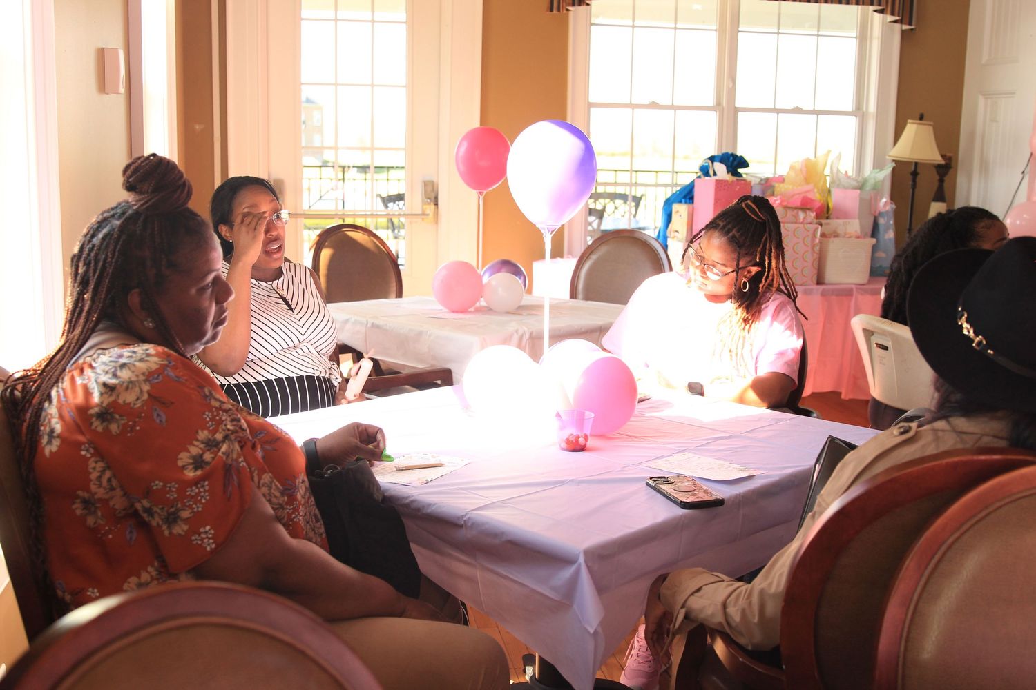 Group of women sitting at a decorated table with pink and purple balloons at a party.