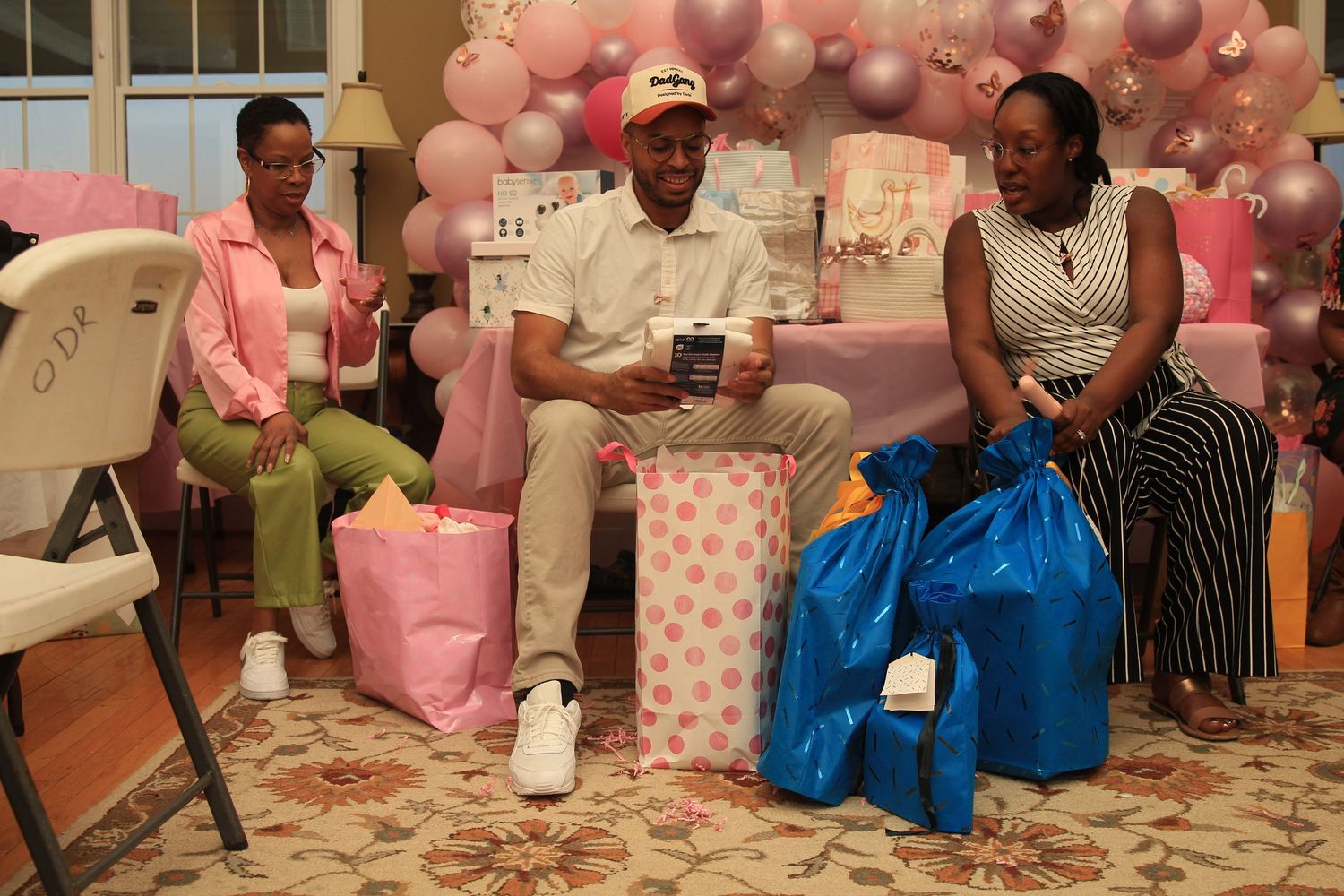 Three people sitting together at a pink baby shower opening gifts and packages.