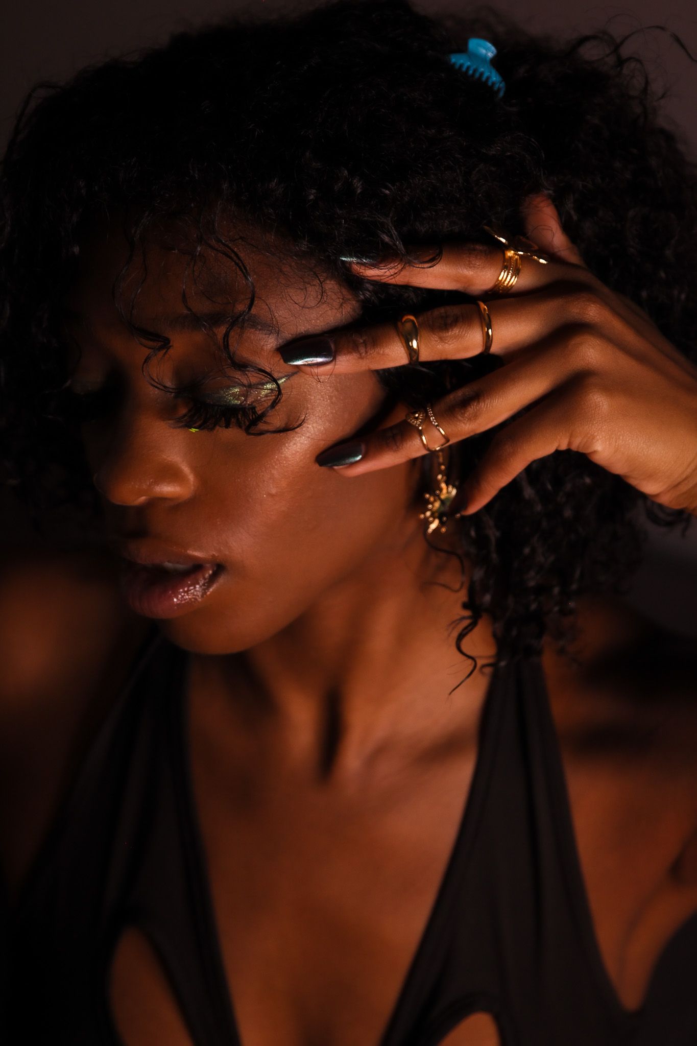 Close-up portrait of a woman with curly hair and gold rings in dramatic lighting.
