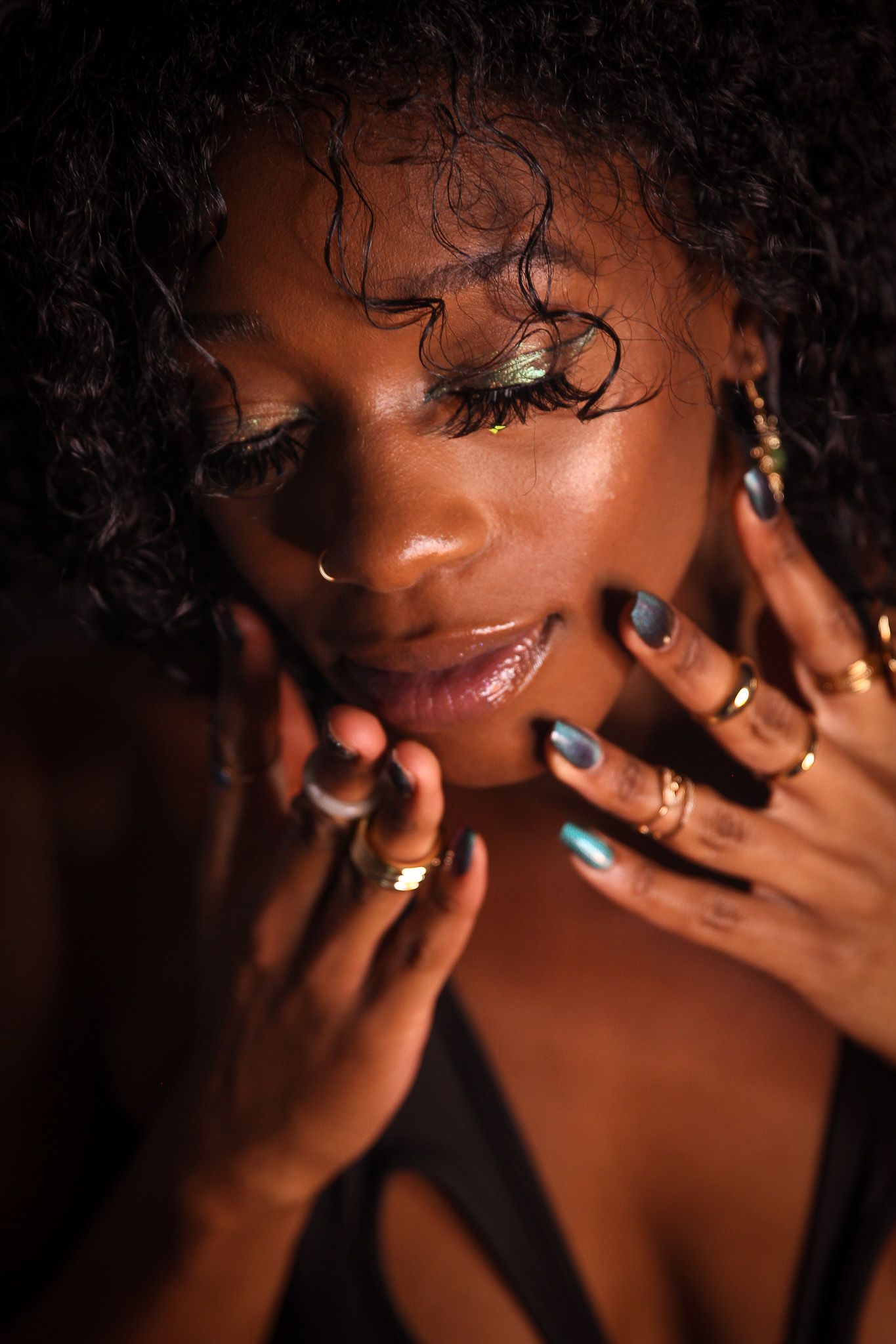 Close-up portrait of Black woman with colorful eye makeup and rings framing her glowing face.