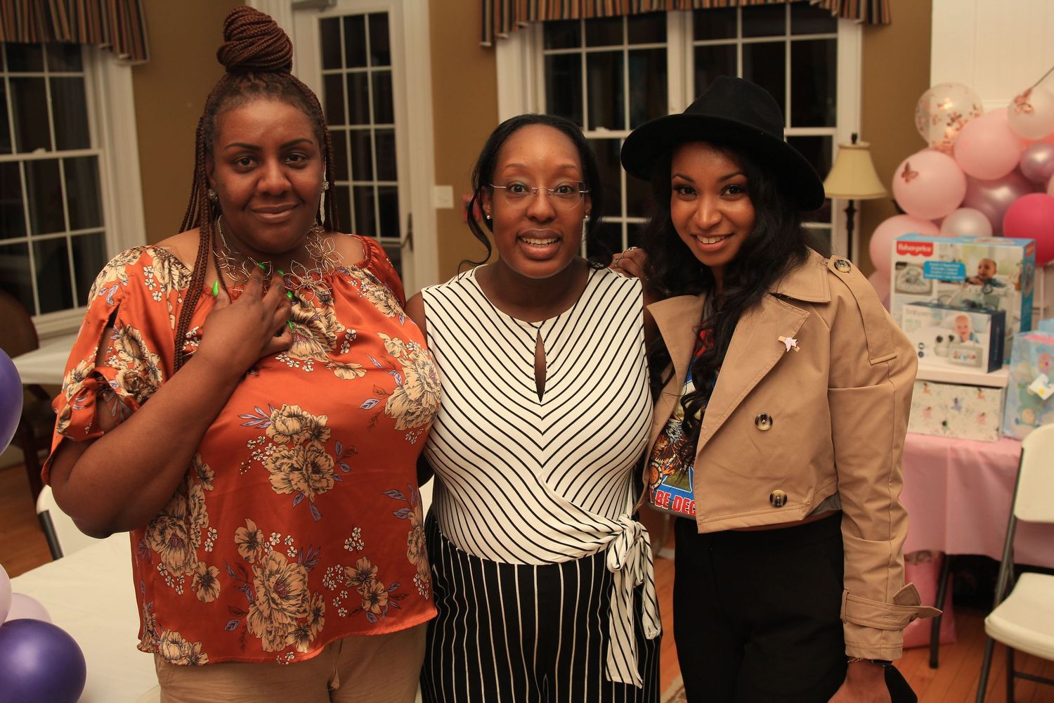 Three women posing together and smiling at a pink-themed baby shower celebration.