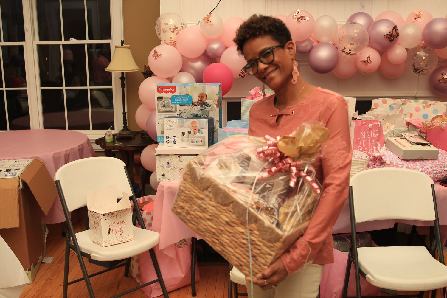 Woman proudly displays a large gift basket at a pink-decorated baby shower celebration.