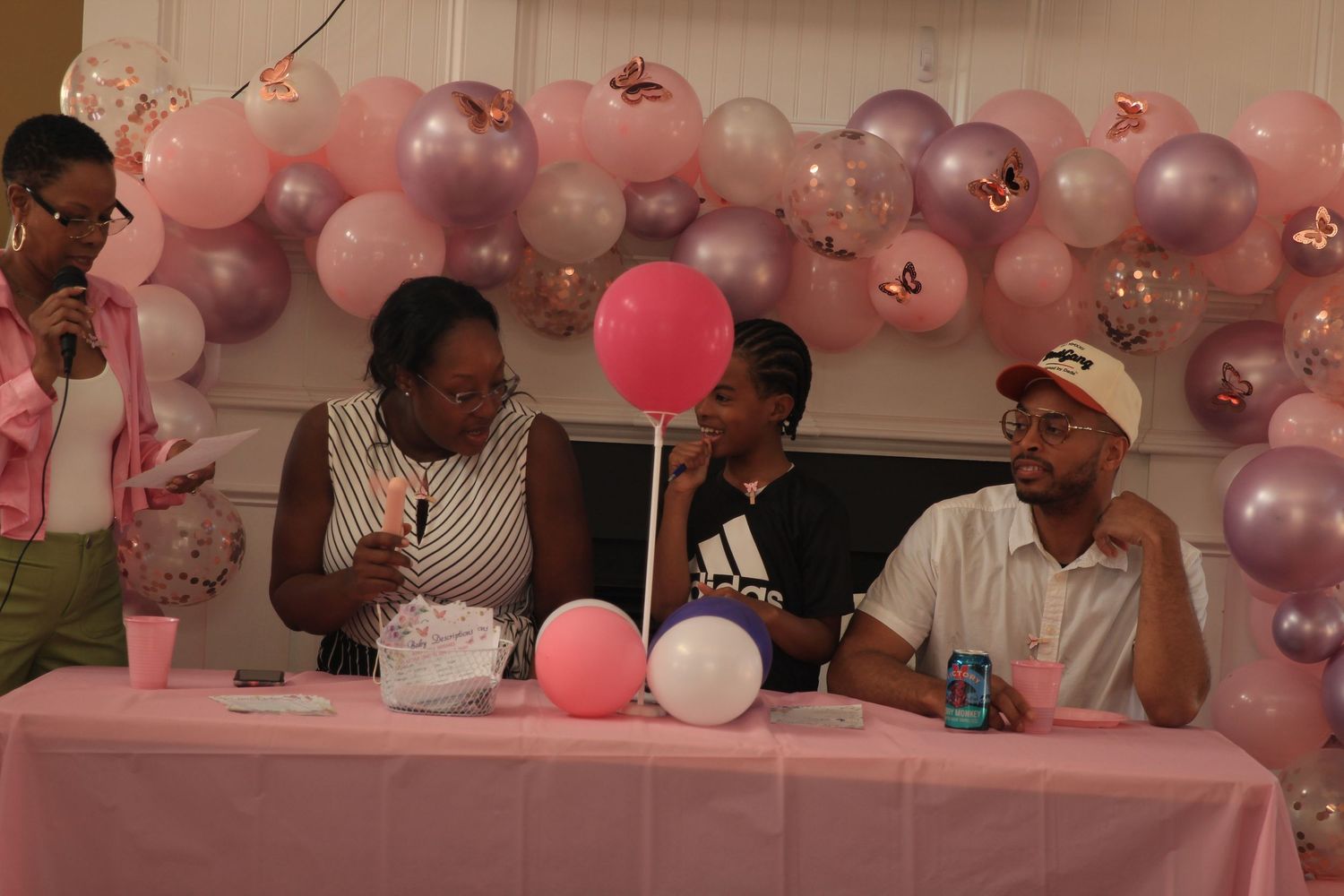 Family members sit together at a pink balloon-decorated baby shower table.