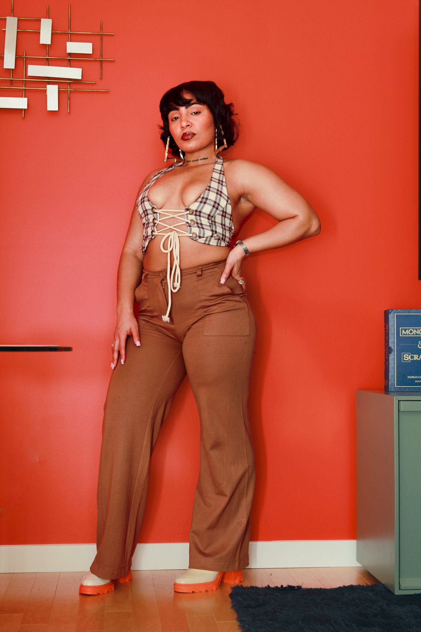 Woman posing in plaid crop top and brown wide-leg pants against a vibrant red wall.