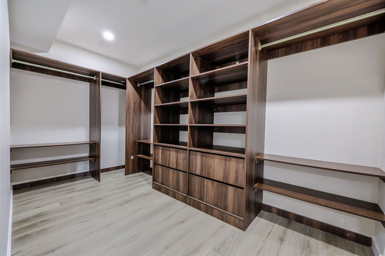 Spacious walk-in closet with dark walnut wood shelving, built-in drawers, and light hardwood flooring.