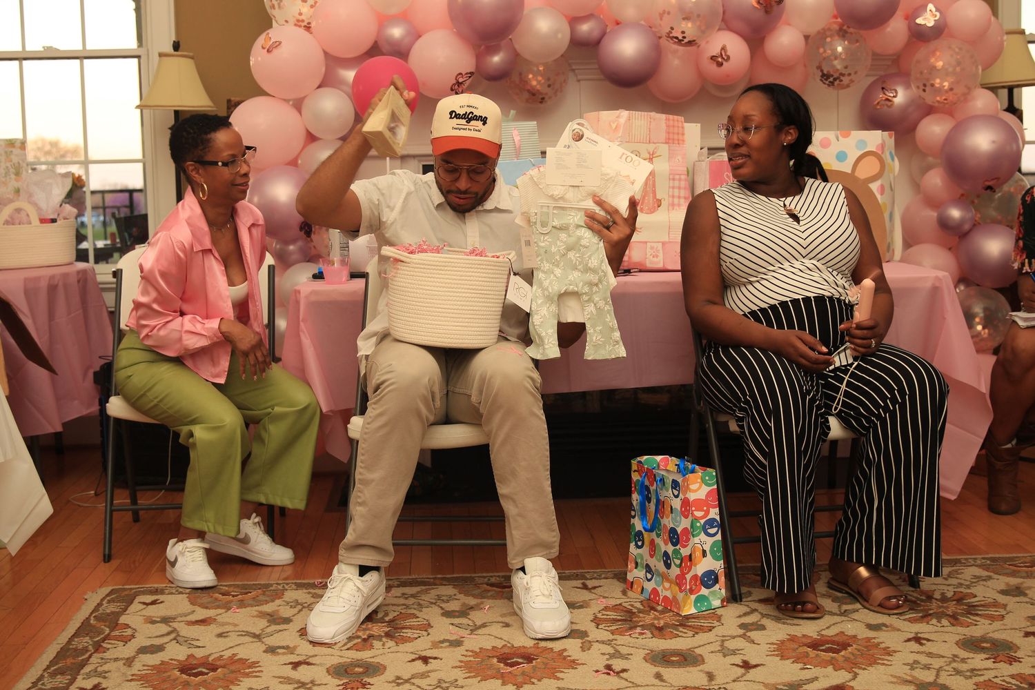 Couple joyfully opens baby shower gifts surrounded by pink decorations.
