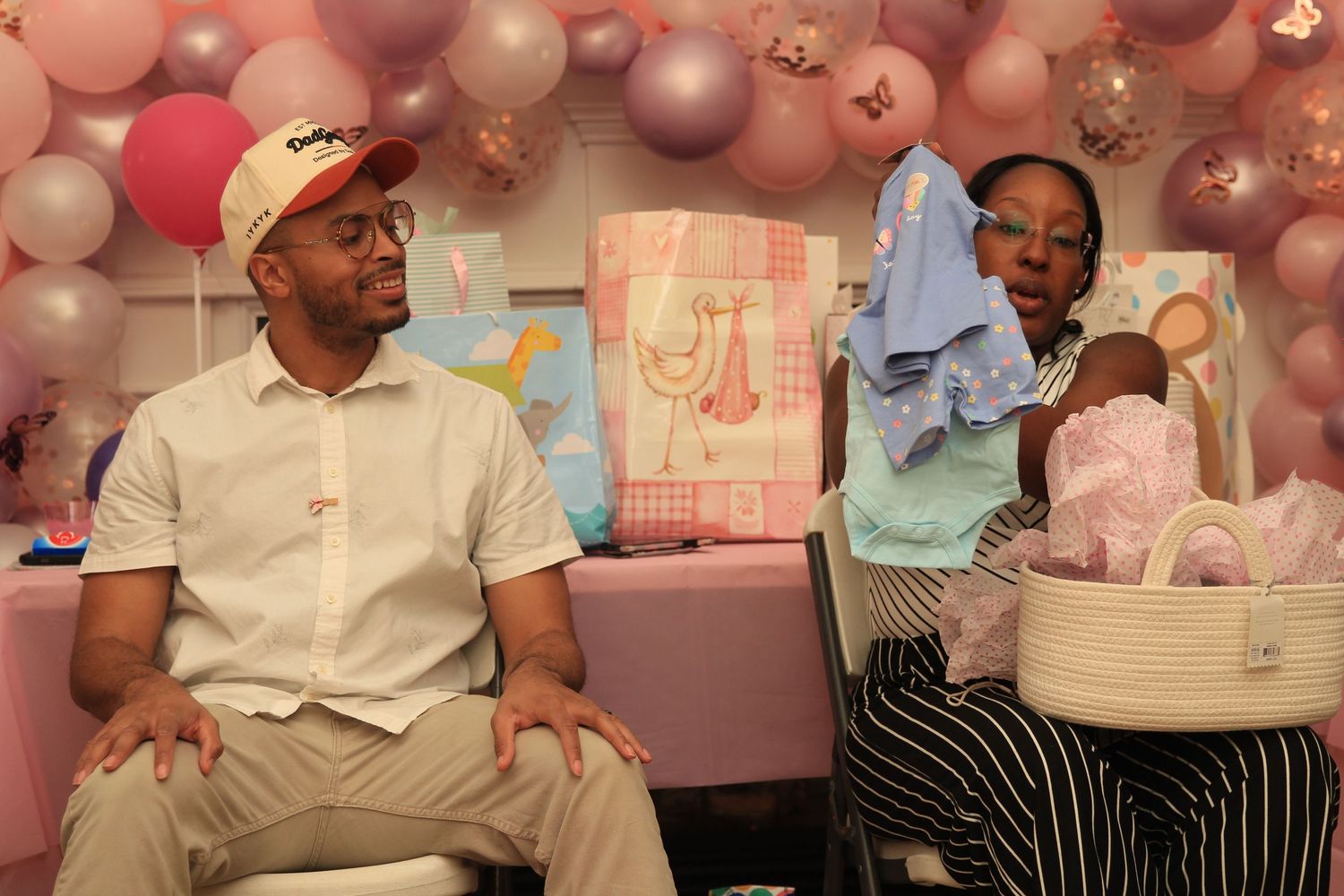 Couple sits together as woman holds baby clothing at a pink shower.