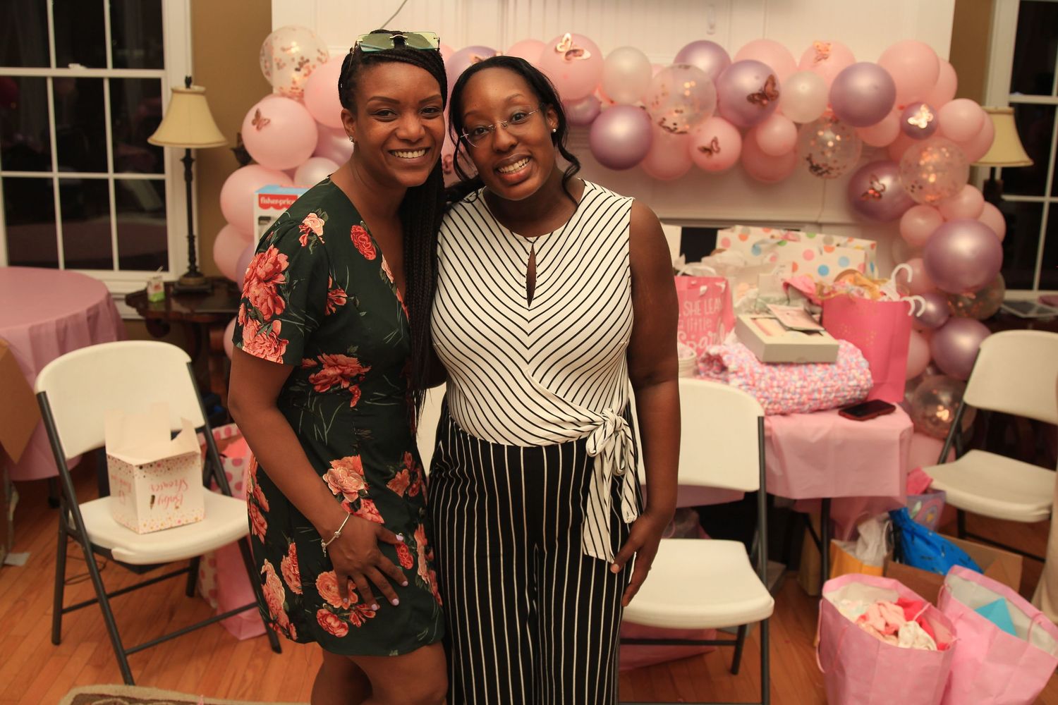 Two women smiling together in front of a pink and purple balloon arch at a baby shower.
