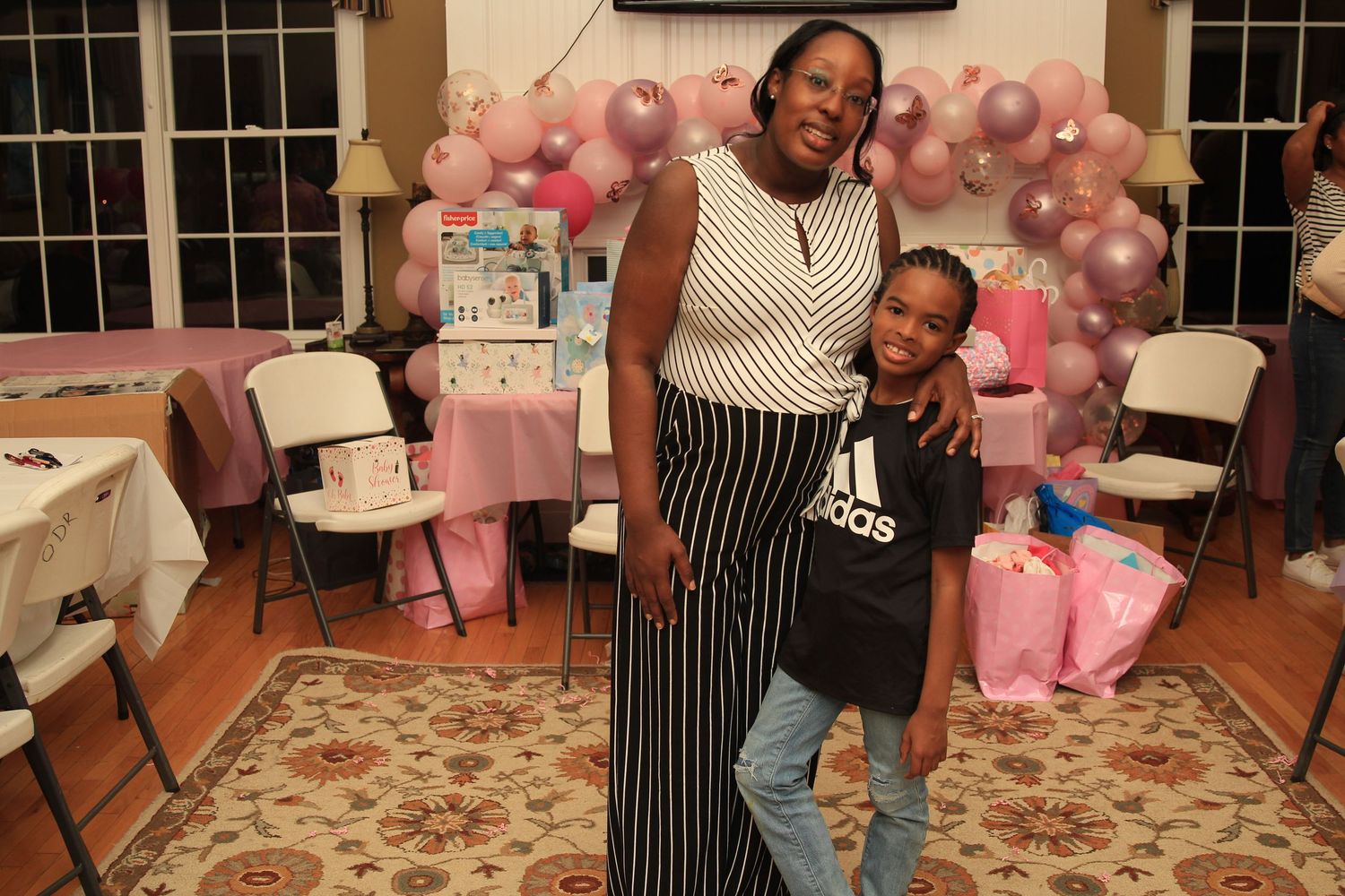 Woman and young boy posing together in front of a pink balloon arch at a baby shower event.
