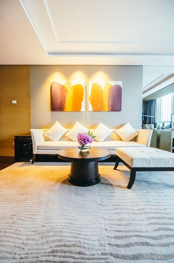 Modern luxury hotel living room with white sofa, round table, and warm wall art.