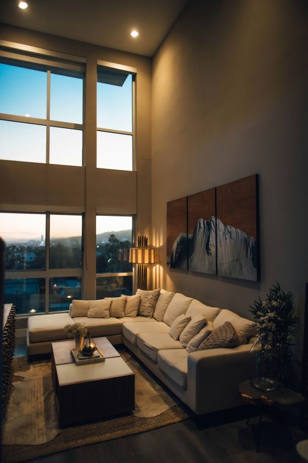 Modern luxury living room with high ceilings, large windows, sectional sofa, and city view at dusk.