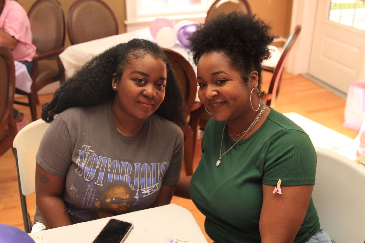 Two women smile warmly together at a table during a baby shower celebration.