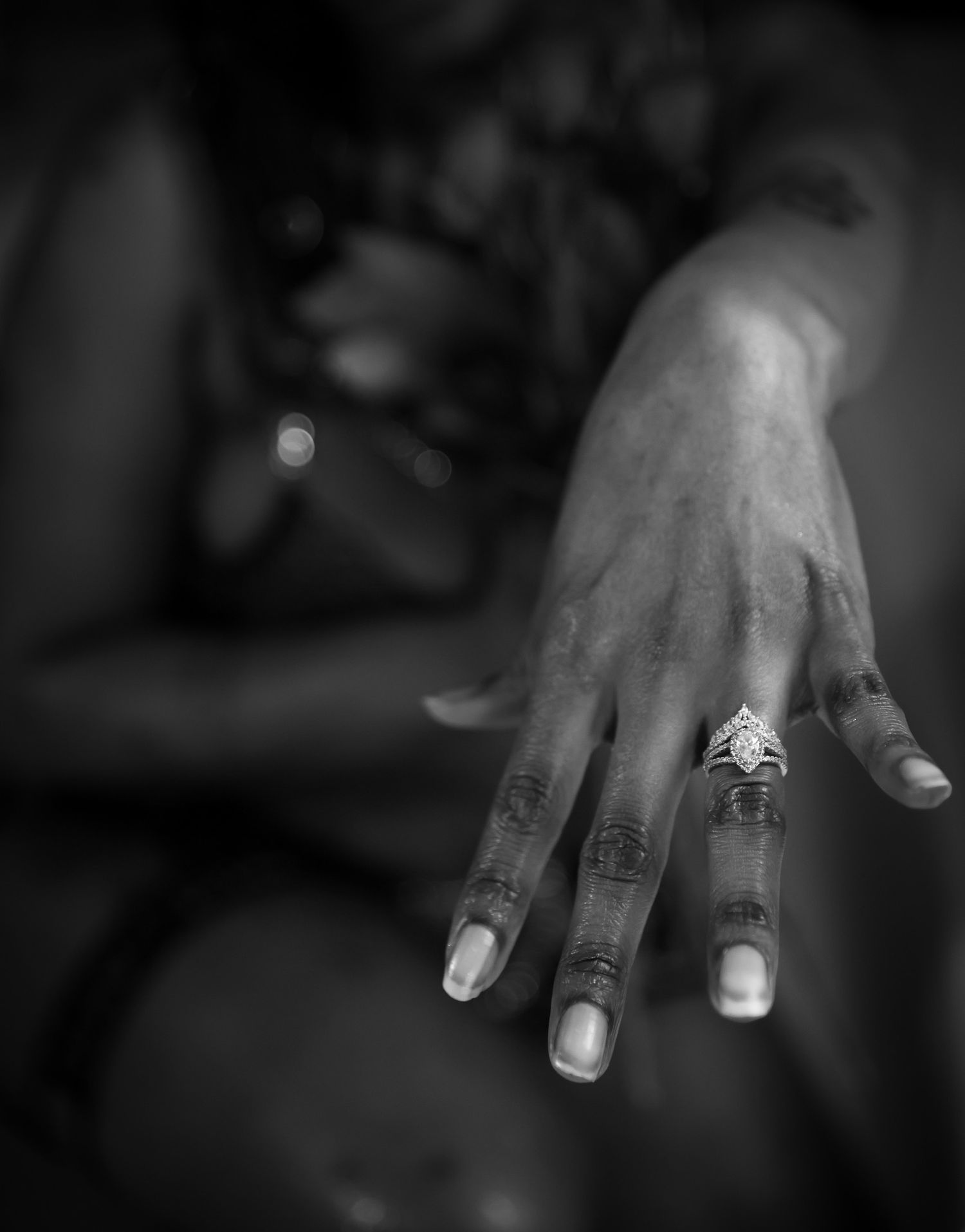 Close-up black and white photo of a hand wearing an elegant diamond engagement ring on the ring finger.