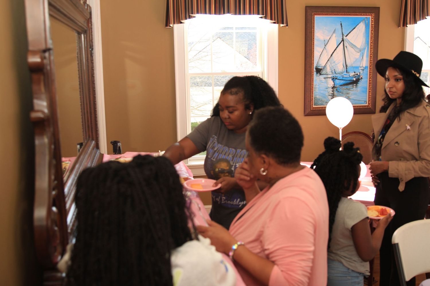 Women socialize and share food at a pink-themed baby shower gathering indoors.