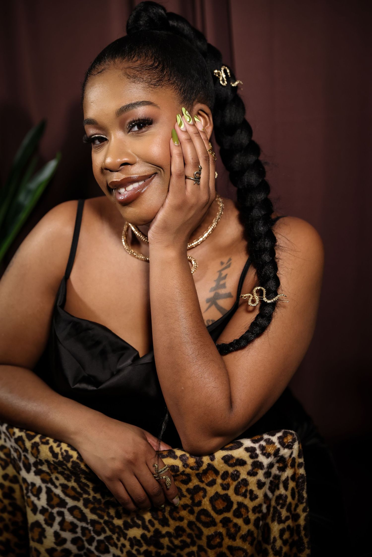 A woman with a long braid and gold jewelry smiles softly while seated on a leopard-print chair.