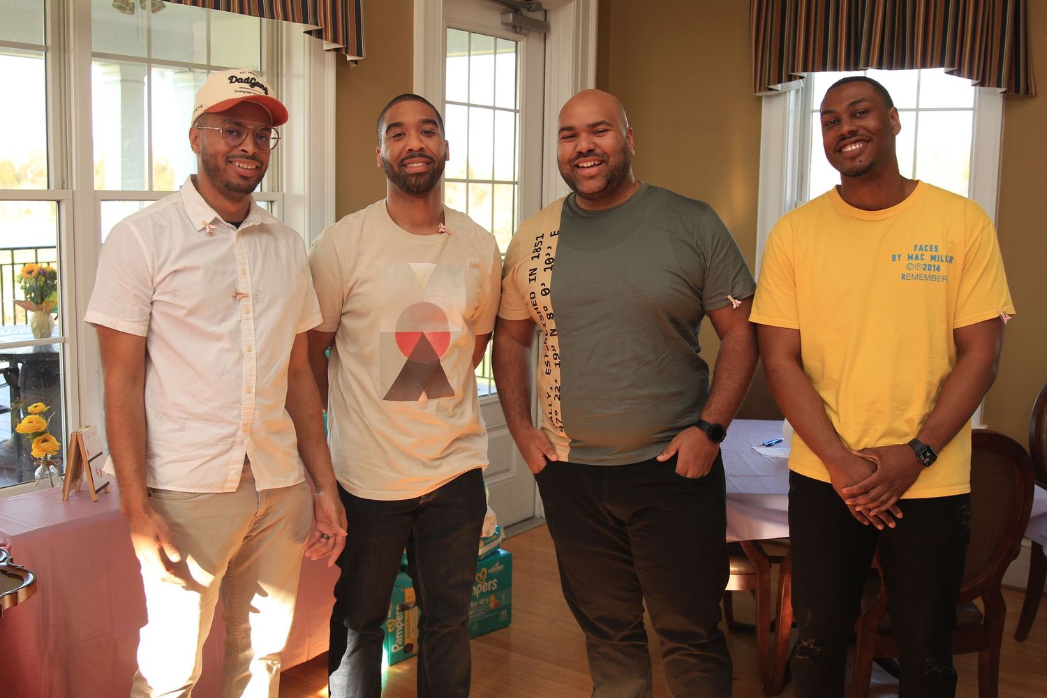Four men smile together for a group photo at an indoor baby shower celebration.