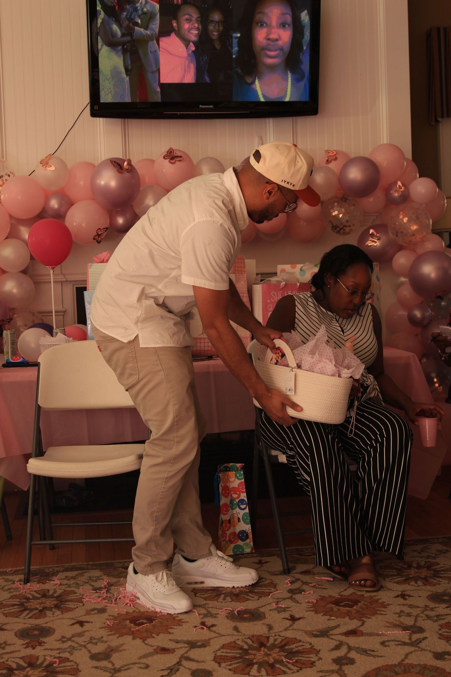 Man presents a gift basket to a woman at a pink baby shower.