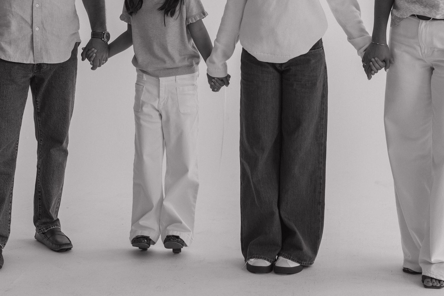 Black and white photo of family holding hands together, showing lower half of bodies.