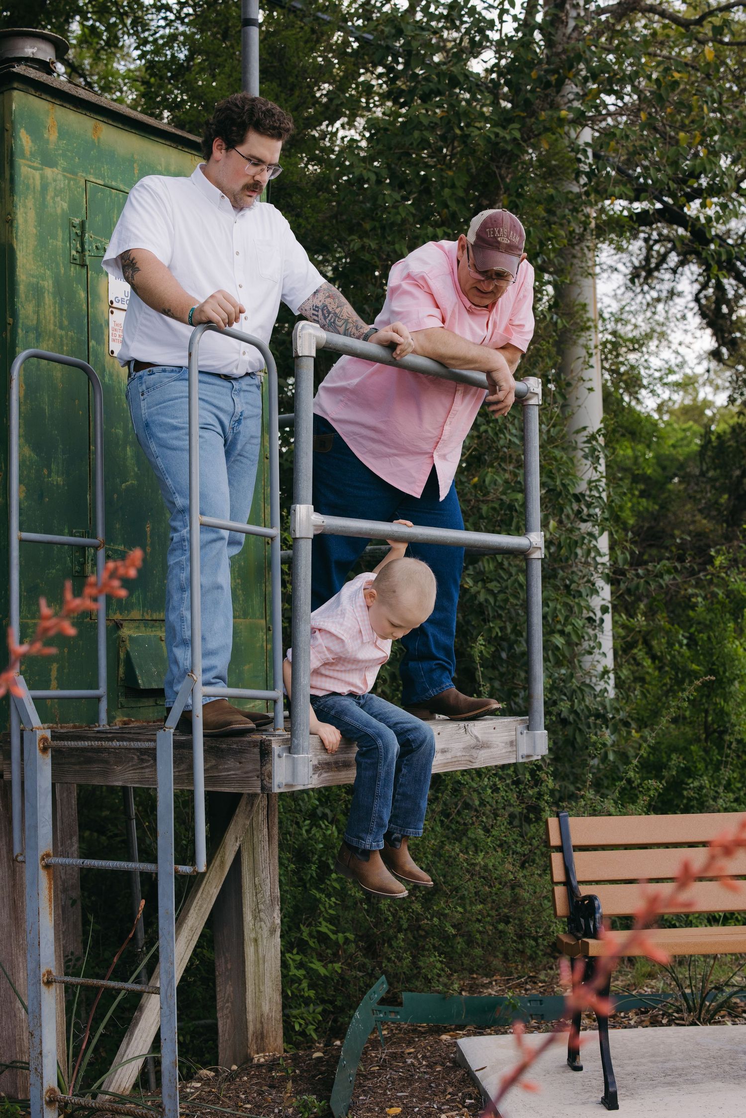 Two adults helping a young child climb down metal playground equipment outdoors.