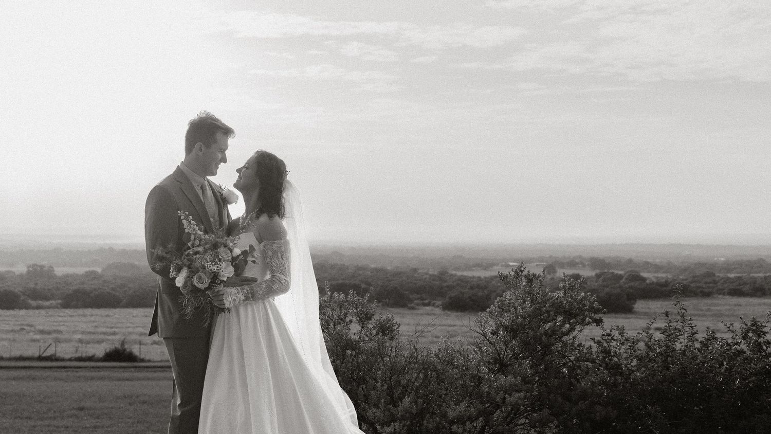 Black and white wedding couple embracing at sunset in open field.