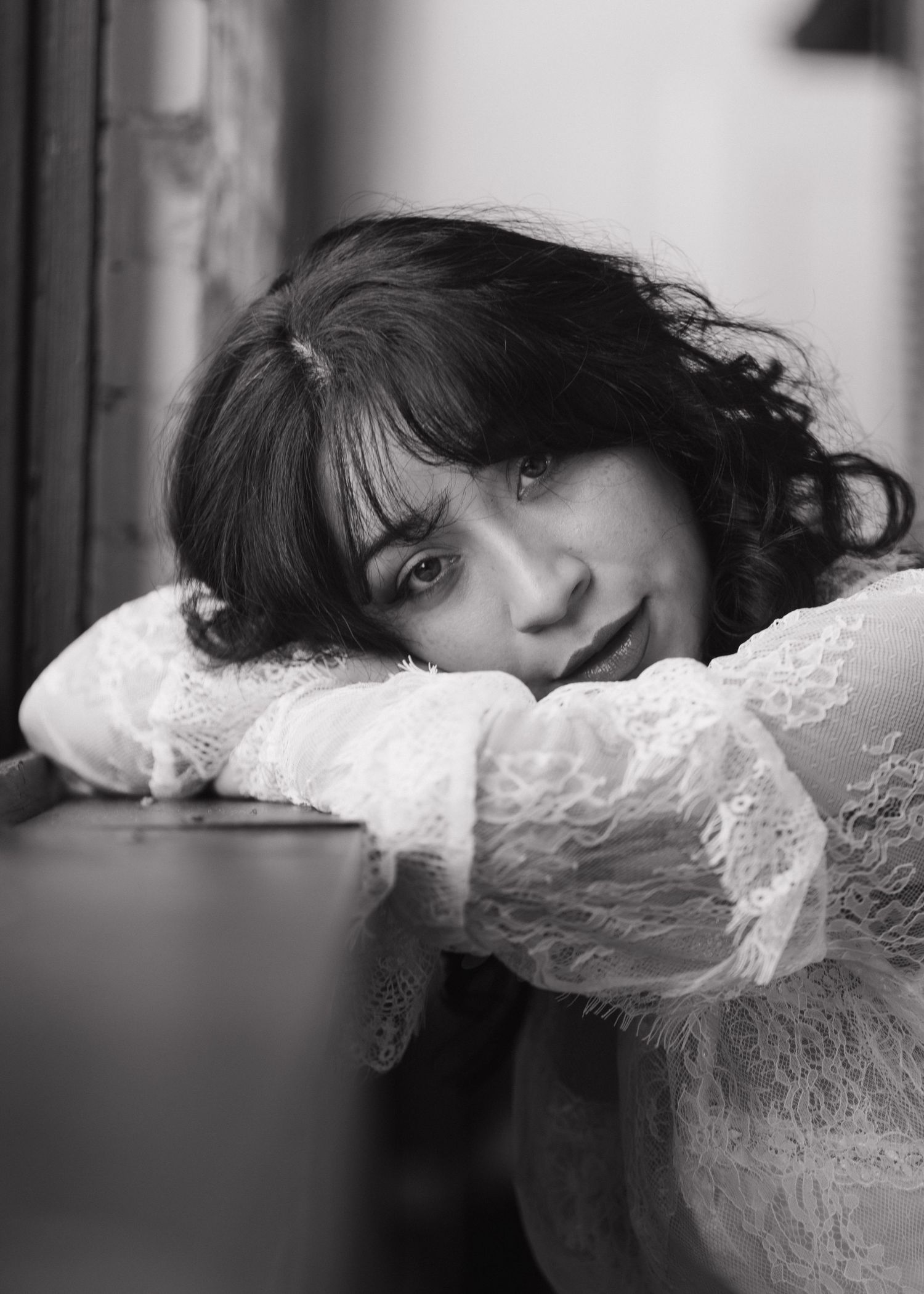 Black and white portrait of curly-haired woman resting chin on arms on surface.
