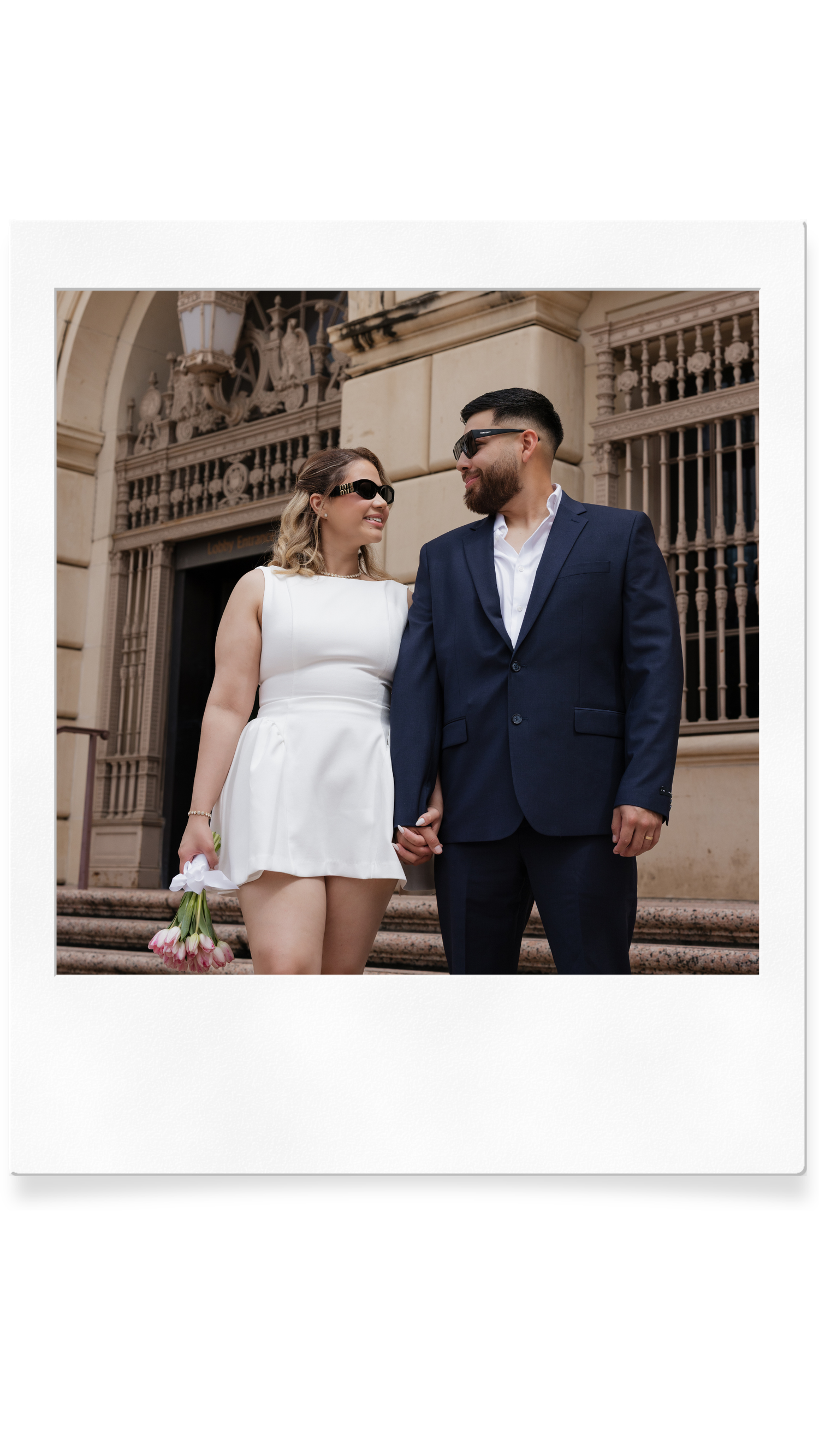 Couple in wedding attire holding hands outside a historic building in a Polaroid frame.
