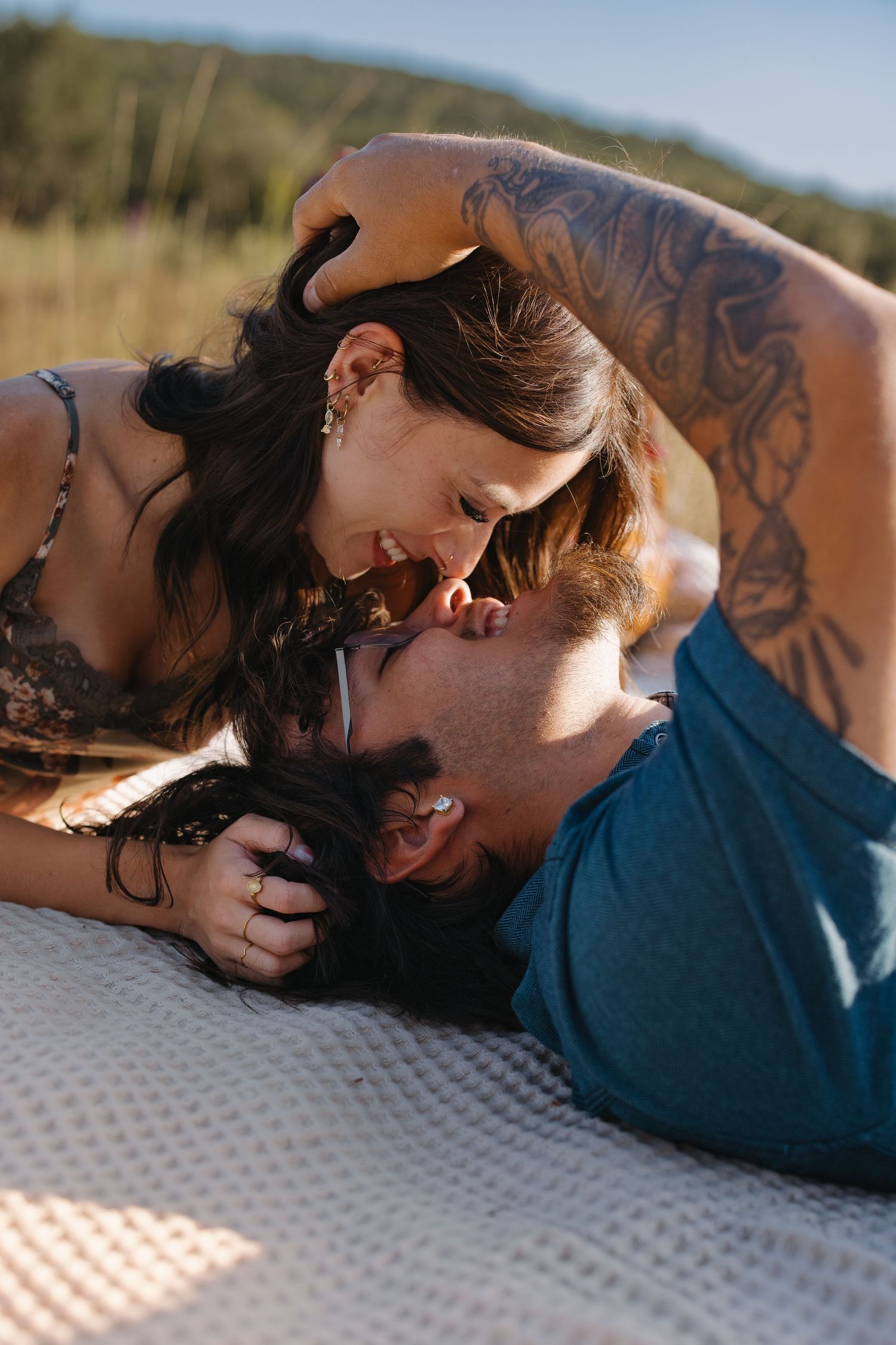 Romantic couple lying on blanket outdoors, nearly kissing in natural sunlit setting.