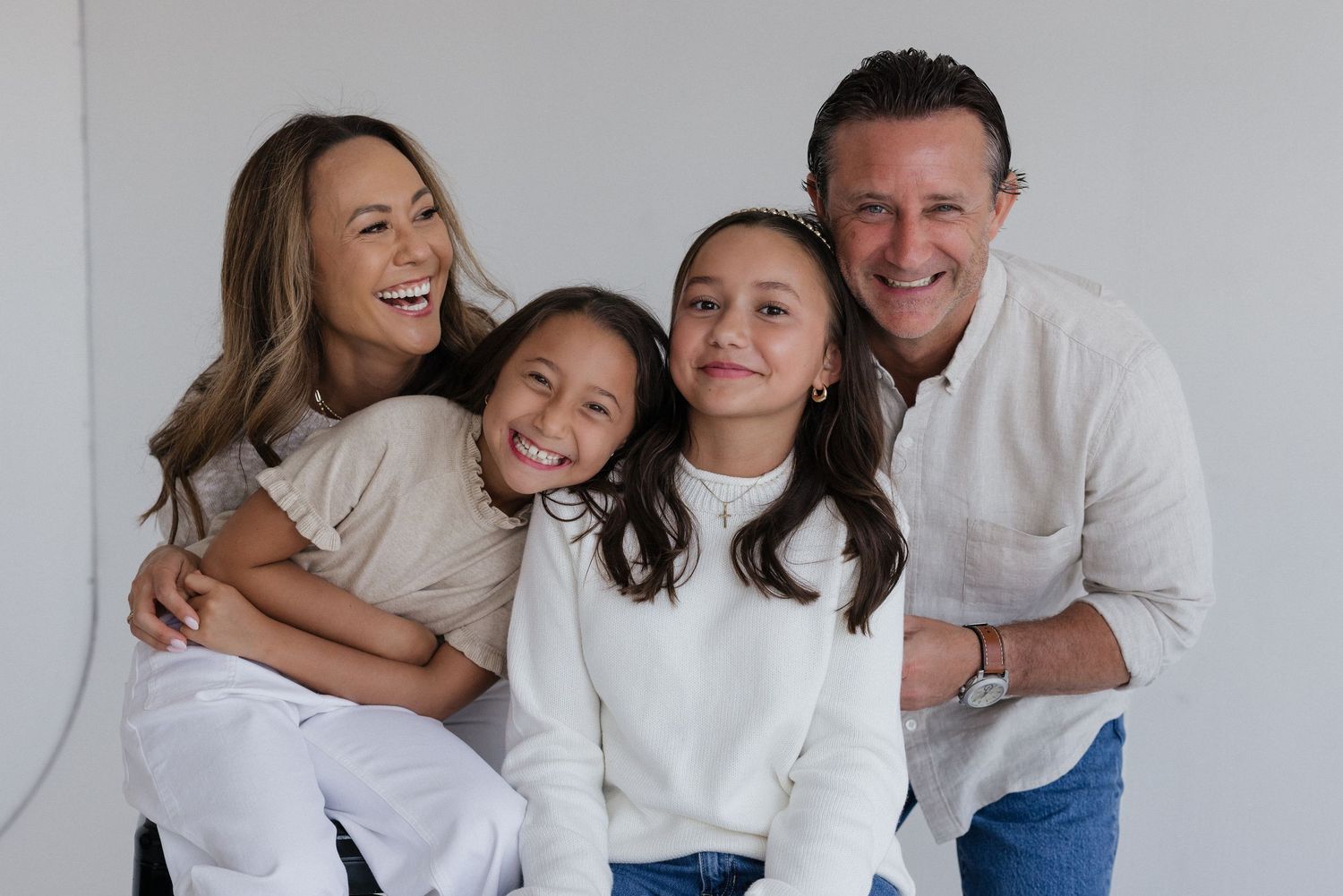 family of four smiling together in a bright white studio portrait.
