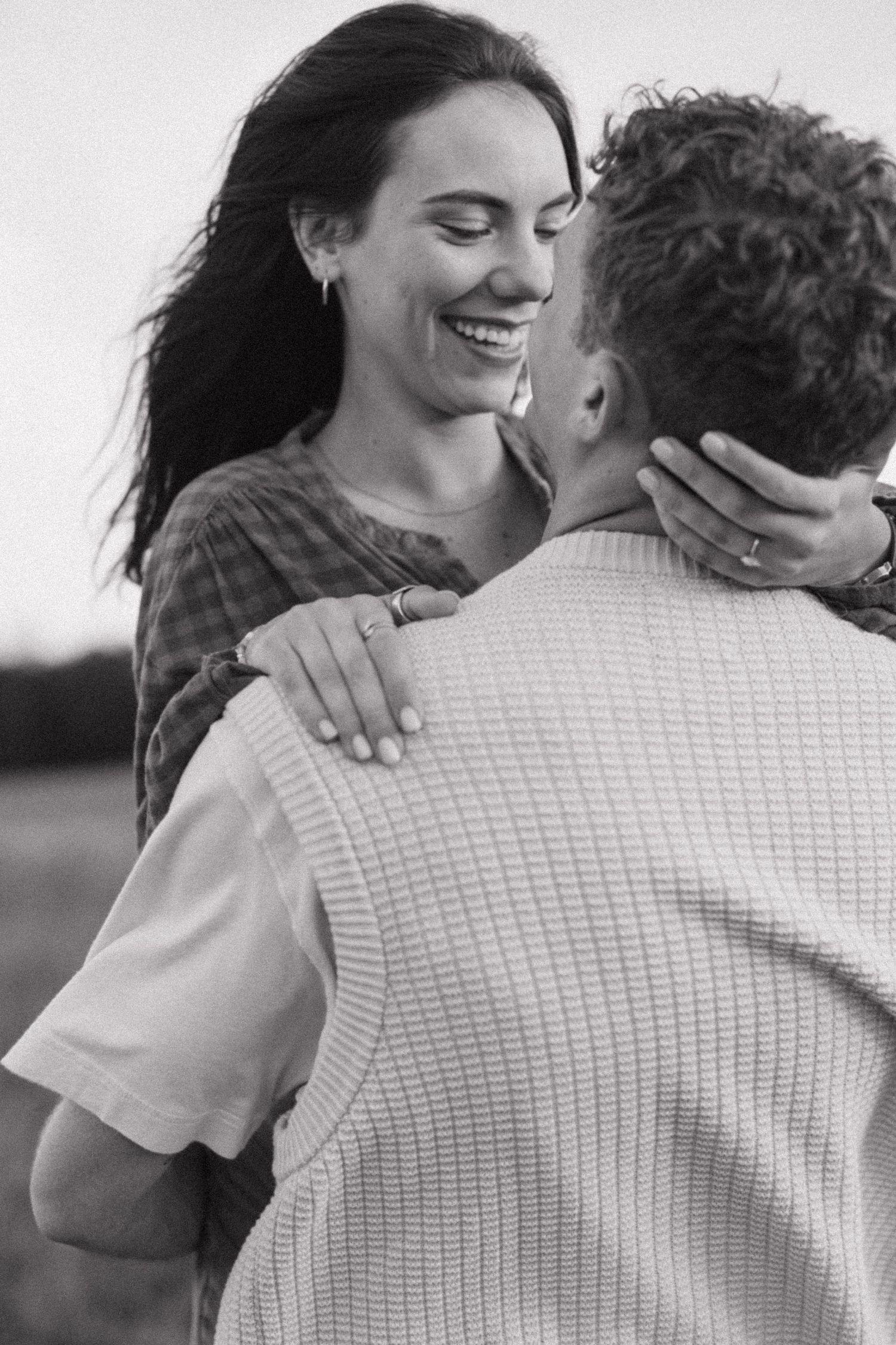 Black and white photo of a smiling woman embracing a man outdoors.