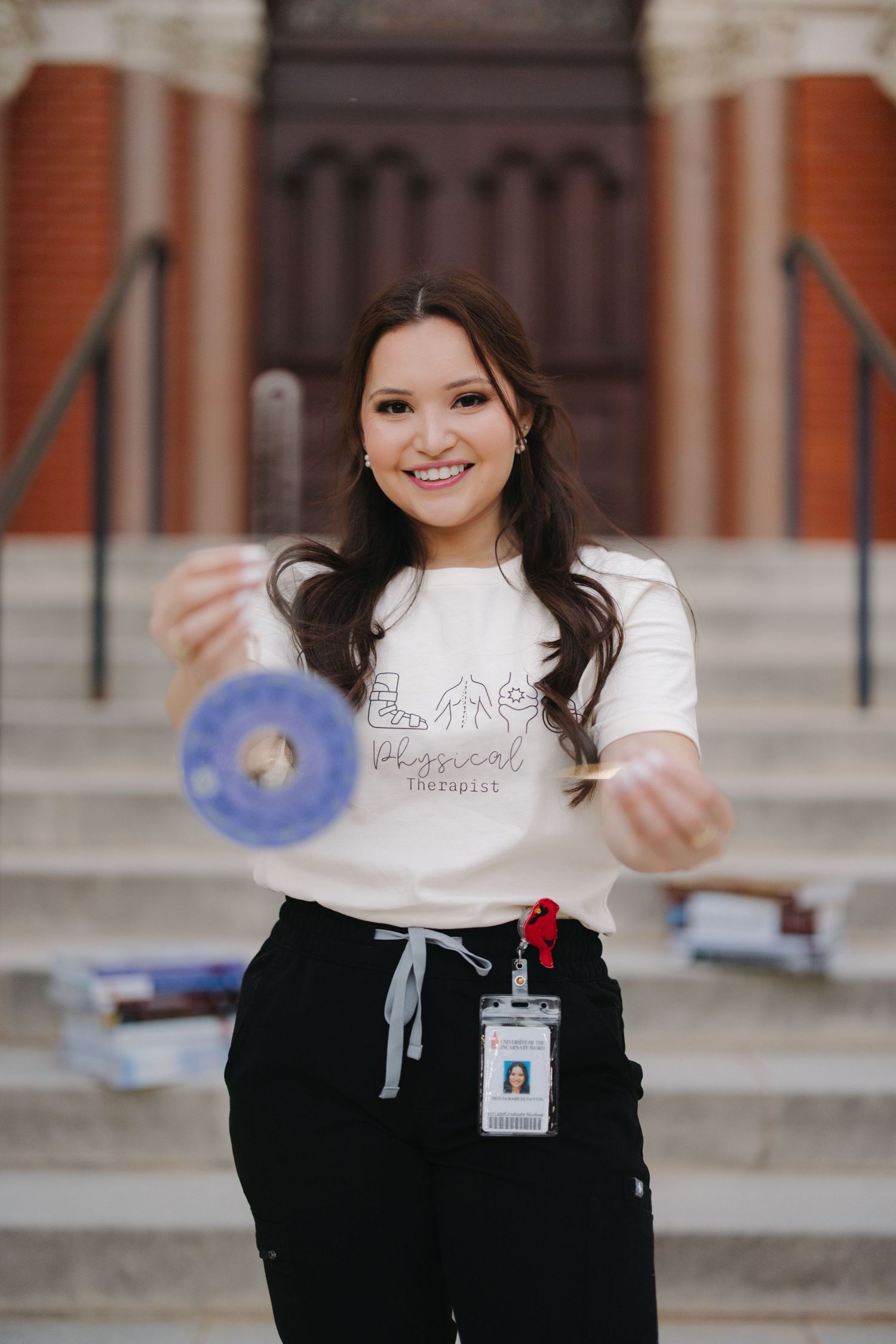 Smiling woman in white physical therapist tee holding athletic tape on building steps.