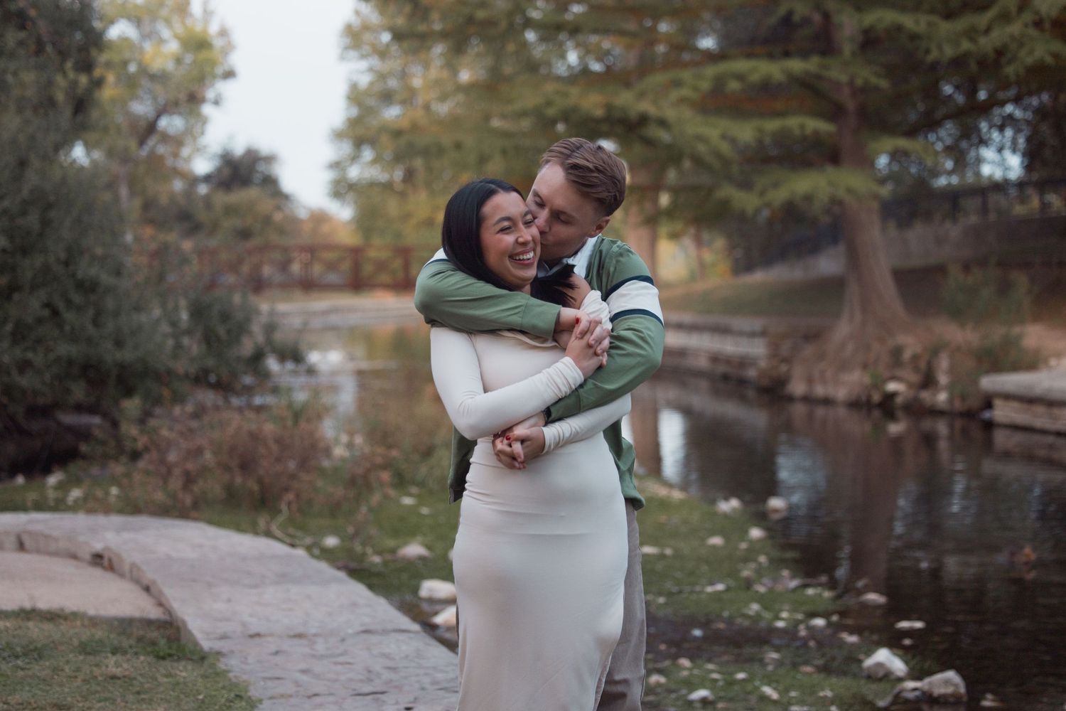 Happy couple embracing and laughing together near a scenic park pond with autumn foliage.