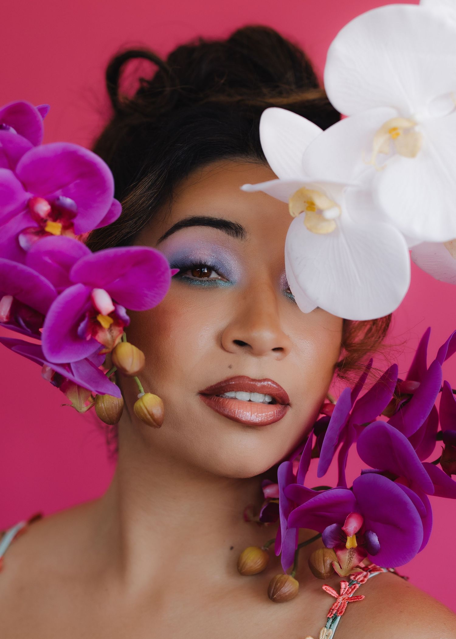 women portraits with purple eye makeup surrounded by vibrant pink and white orchids.