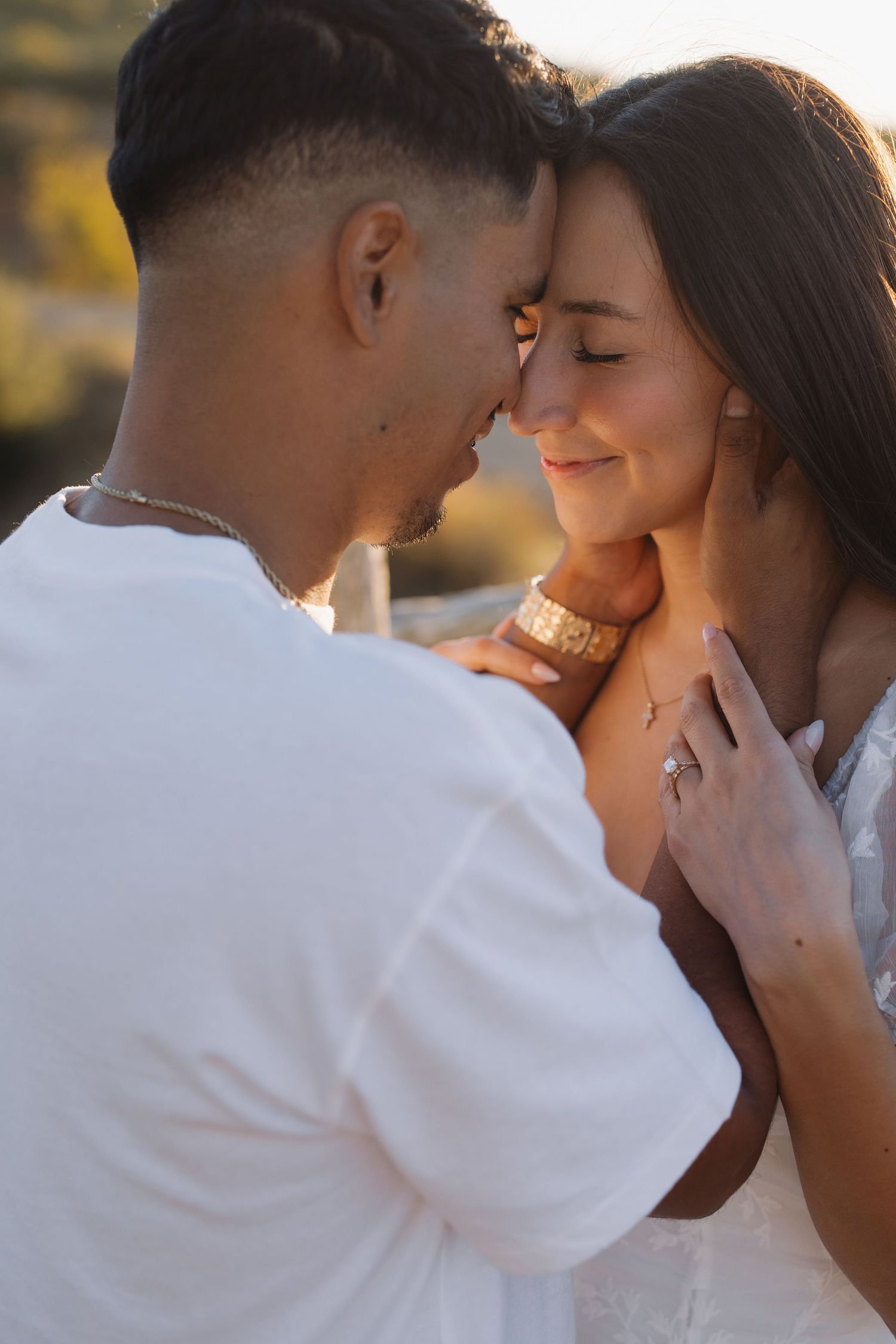 A couple shares a tender romantic moment at golden hour, with the woman smiling softly as the man gently cups her face.
