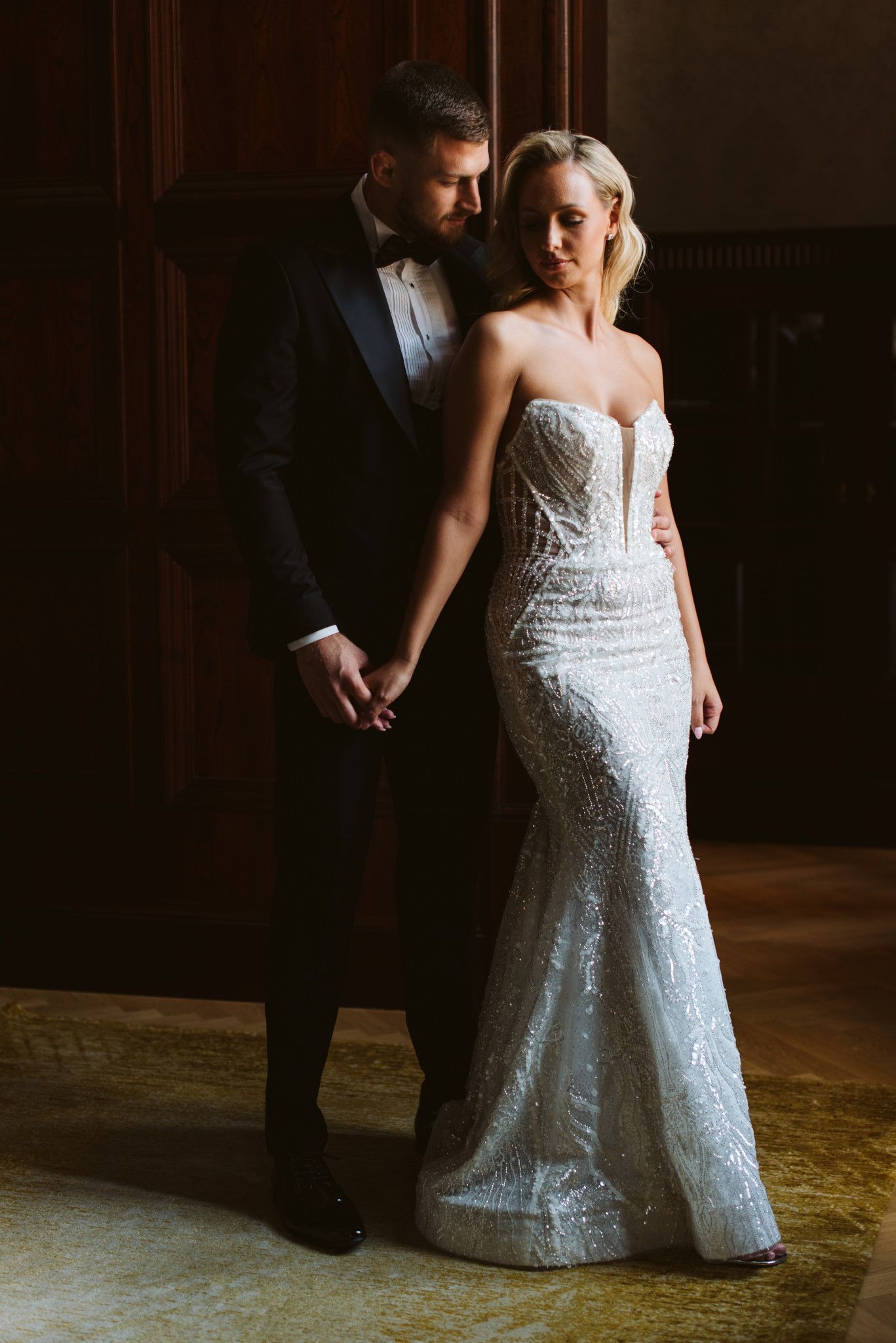 A romantic wedding portrait featuring a couple in formal attire standing against dark wood paneling.