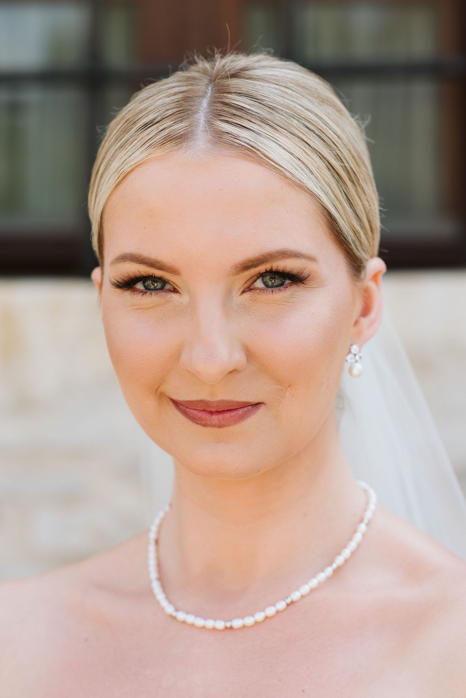 A bride wearing a pearl necklace and natural makeup smiles in an outdoor portrait series.