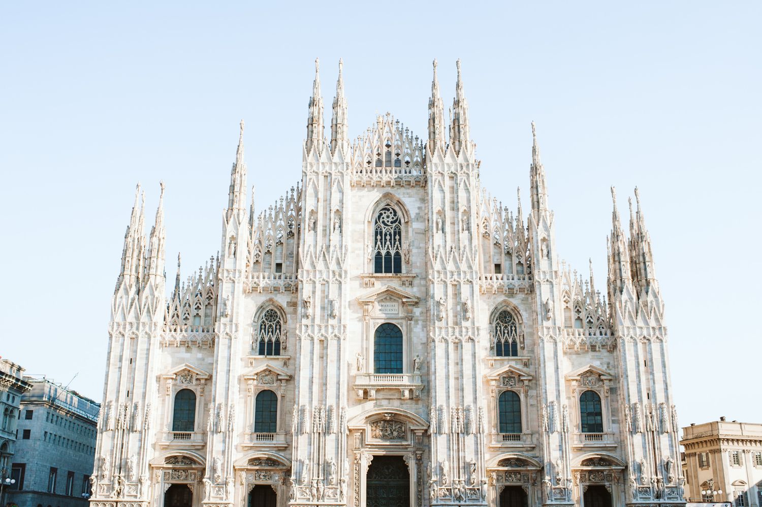 The Milan Cathedral's stunning Gothic facade photographed against a bright blue sky.