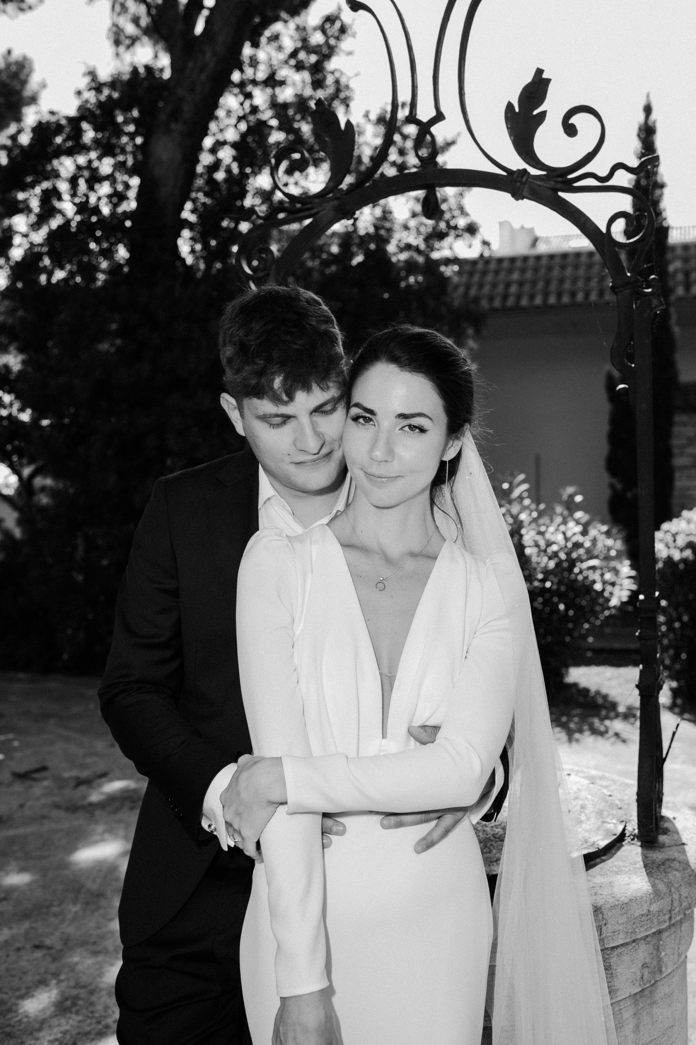An intimate black and white portrait of a couple embracing under an ornate iron archway.