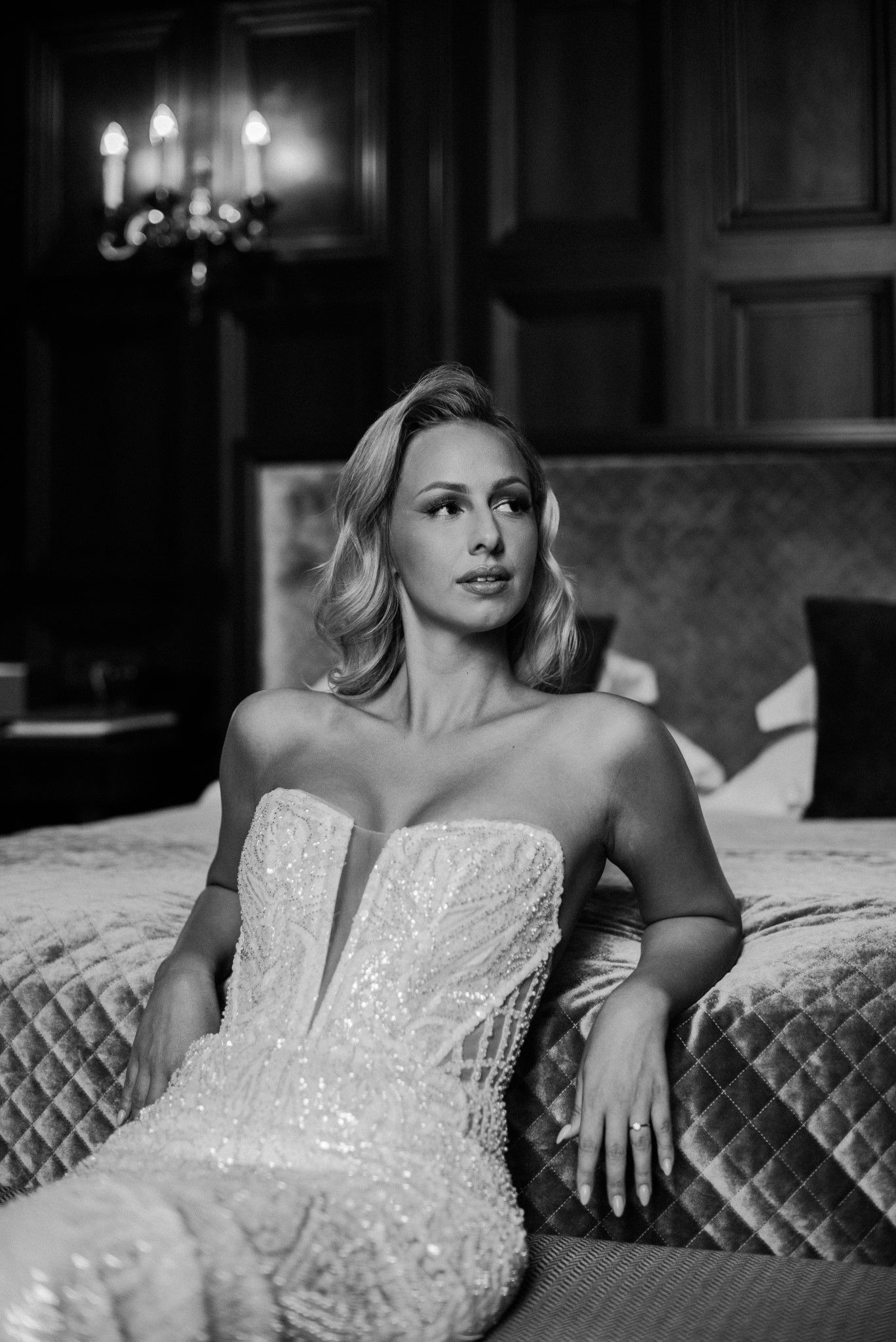 Glamorous bridal portrait on quilted chaise with moody lighting and wooden paneled walls.