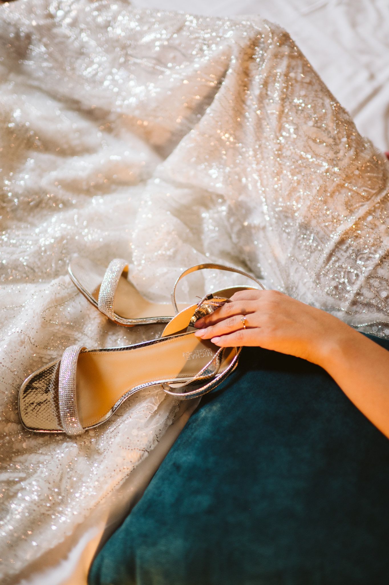 Close-up of sparkly bridal shoes resting on teal velvet fabric.