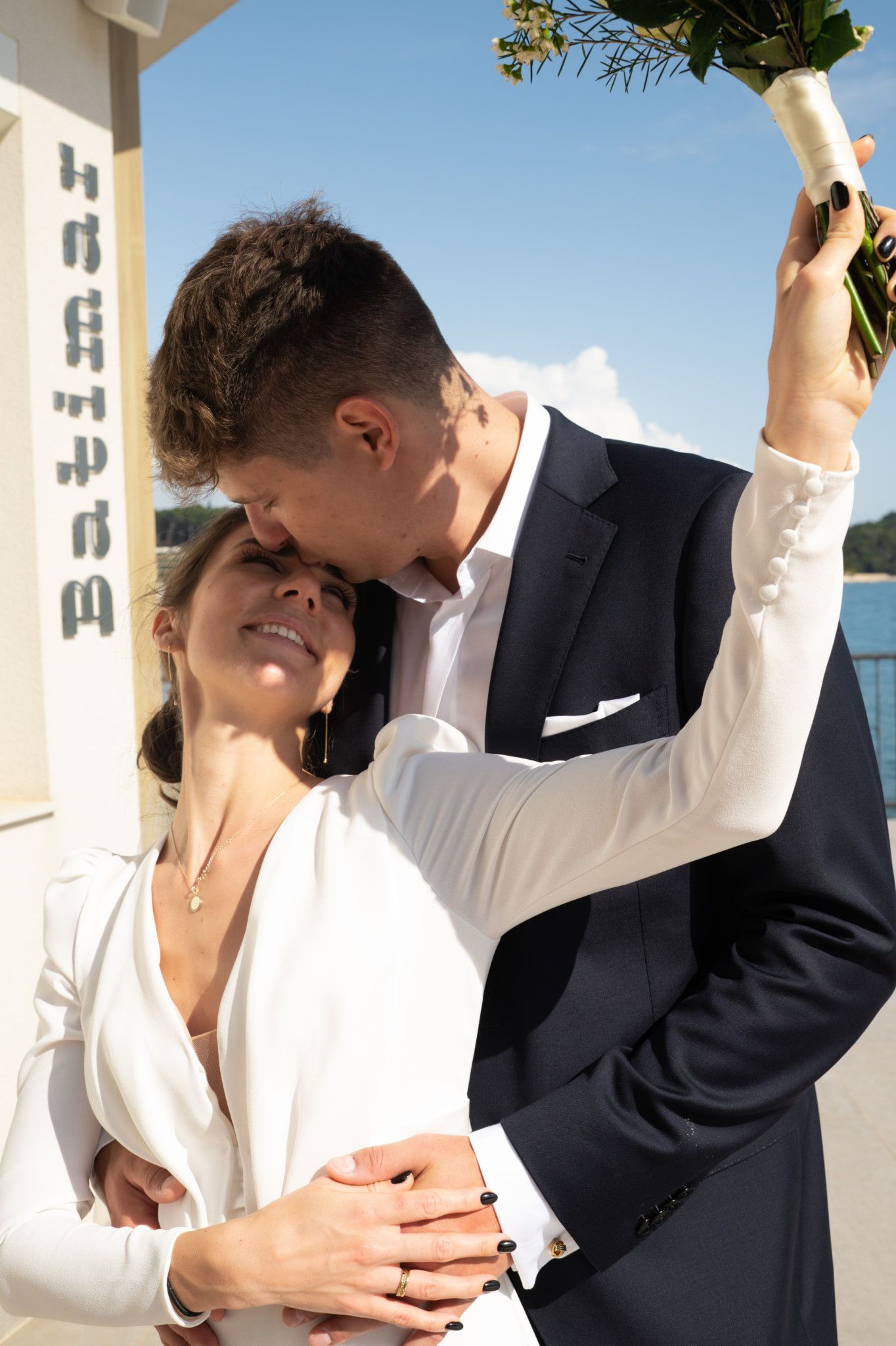 A joyful wedding moment captured as couple embraces under bright blue sky.