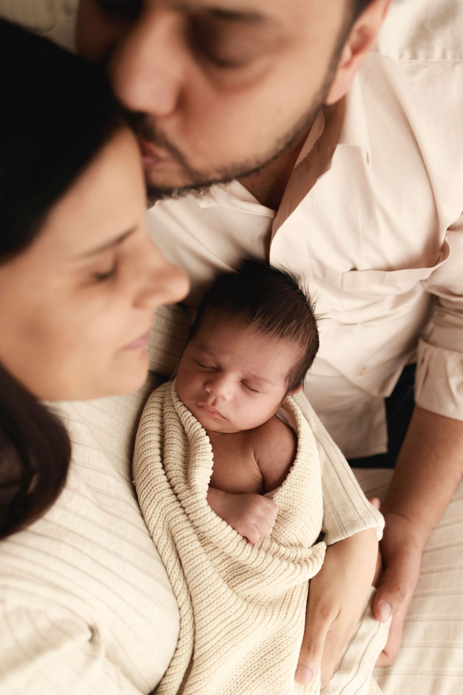 a newborn baby sleeping and wrapped in a beige knitted blanket being held by mother and father