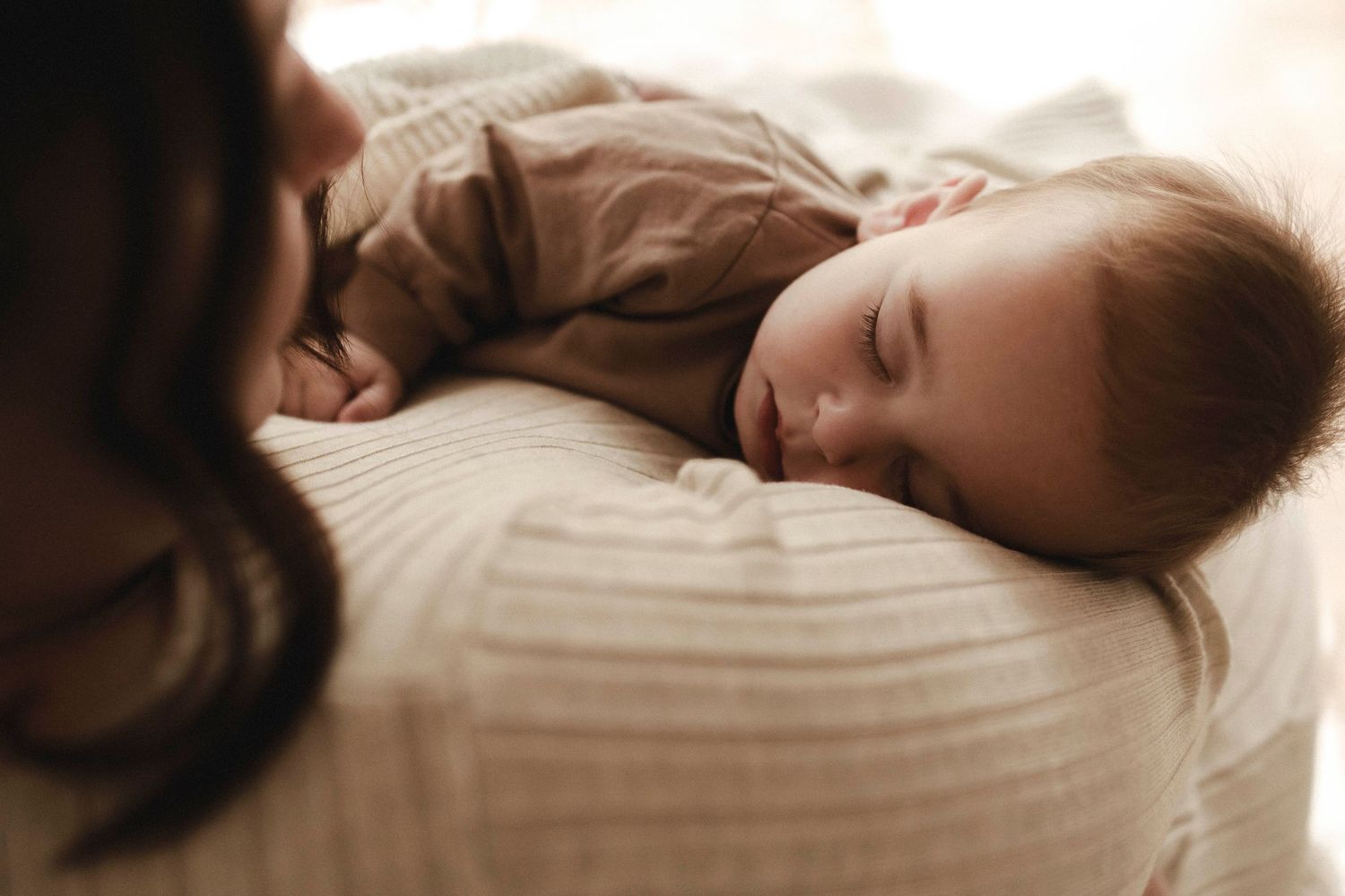 a baby sleeping in mothers arms with camera angled down towards his face and woman looking at him