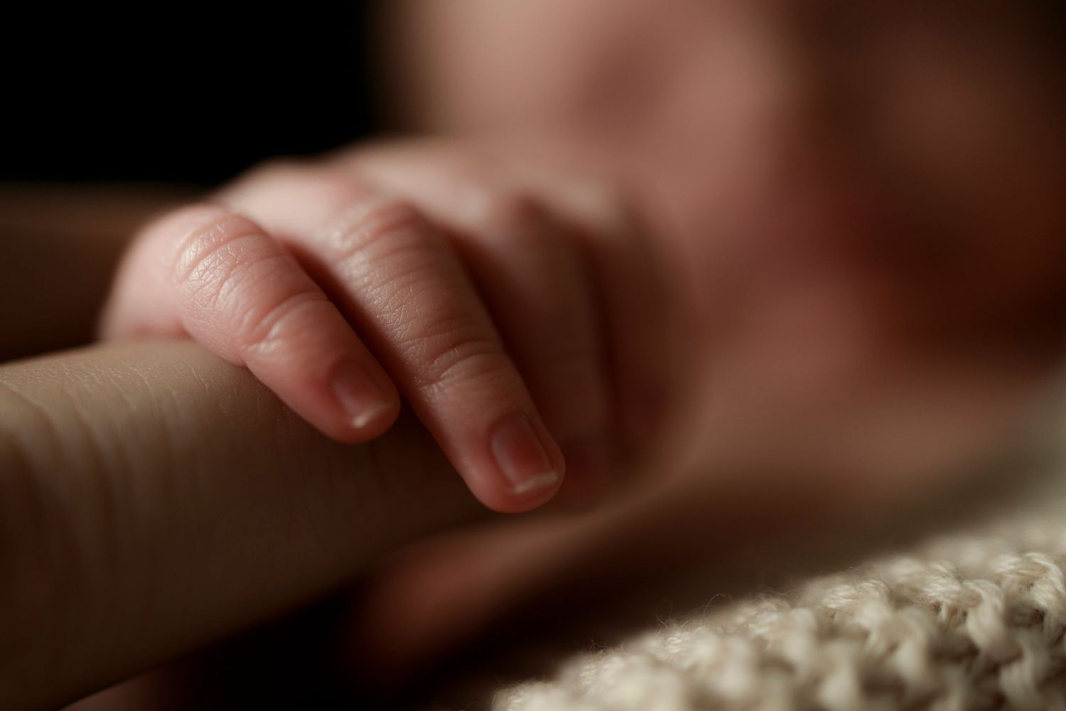 a close up of newborn baby fingers and nails wrapping around parents finger
