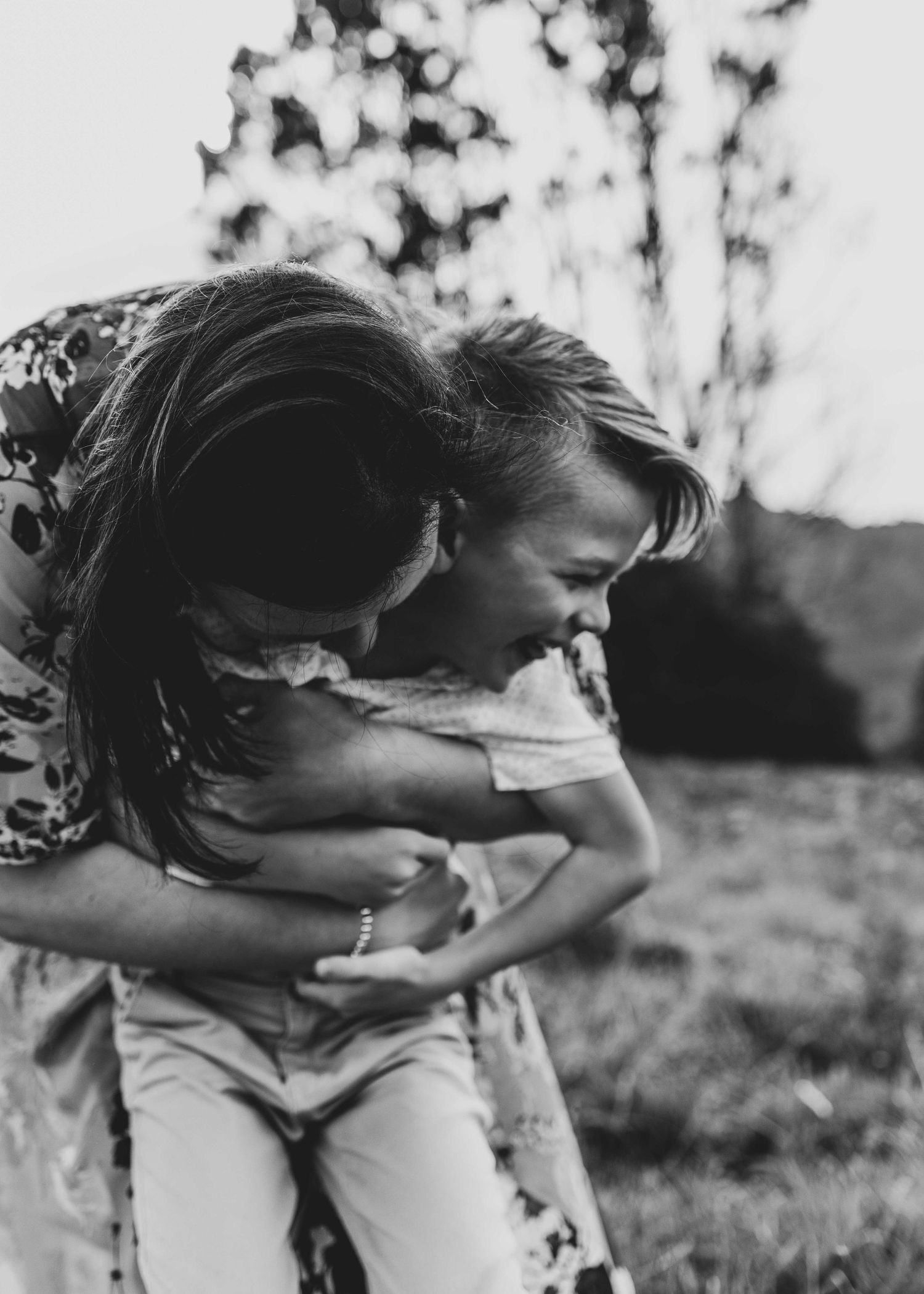 a black and white image of a woman leaning over holding onto a young boy smiling in a grassy field