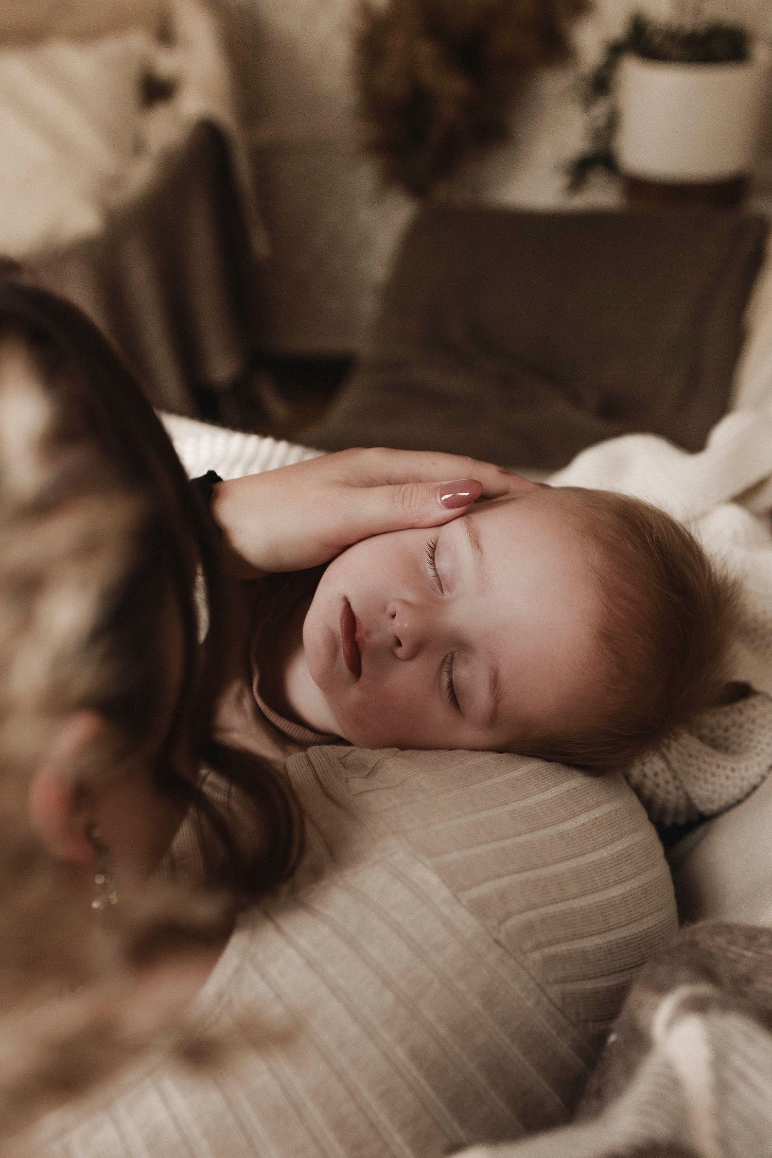 a baby sleeping with face pointing towards the camera whilst being held in the arms of the mother