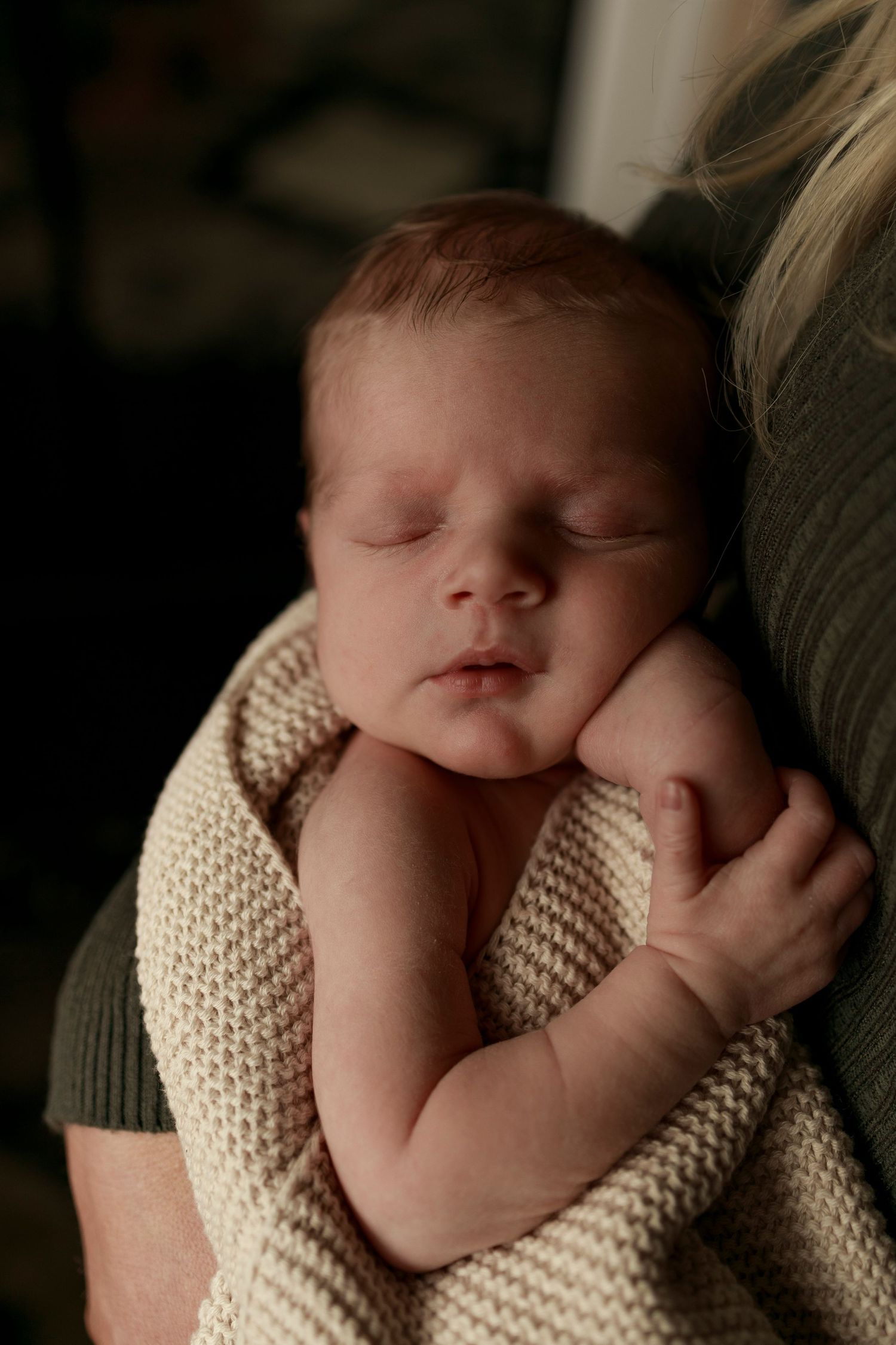 a newborn baby sleeping wrapped in beige knitted blanket being held in mothers arms